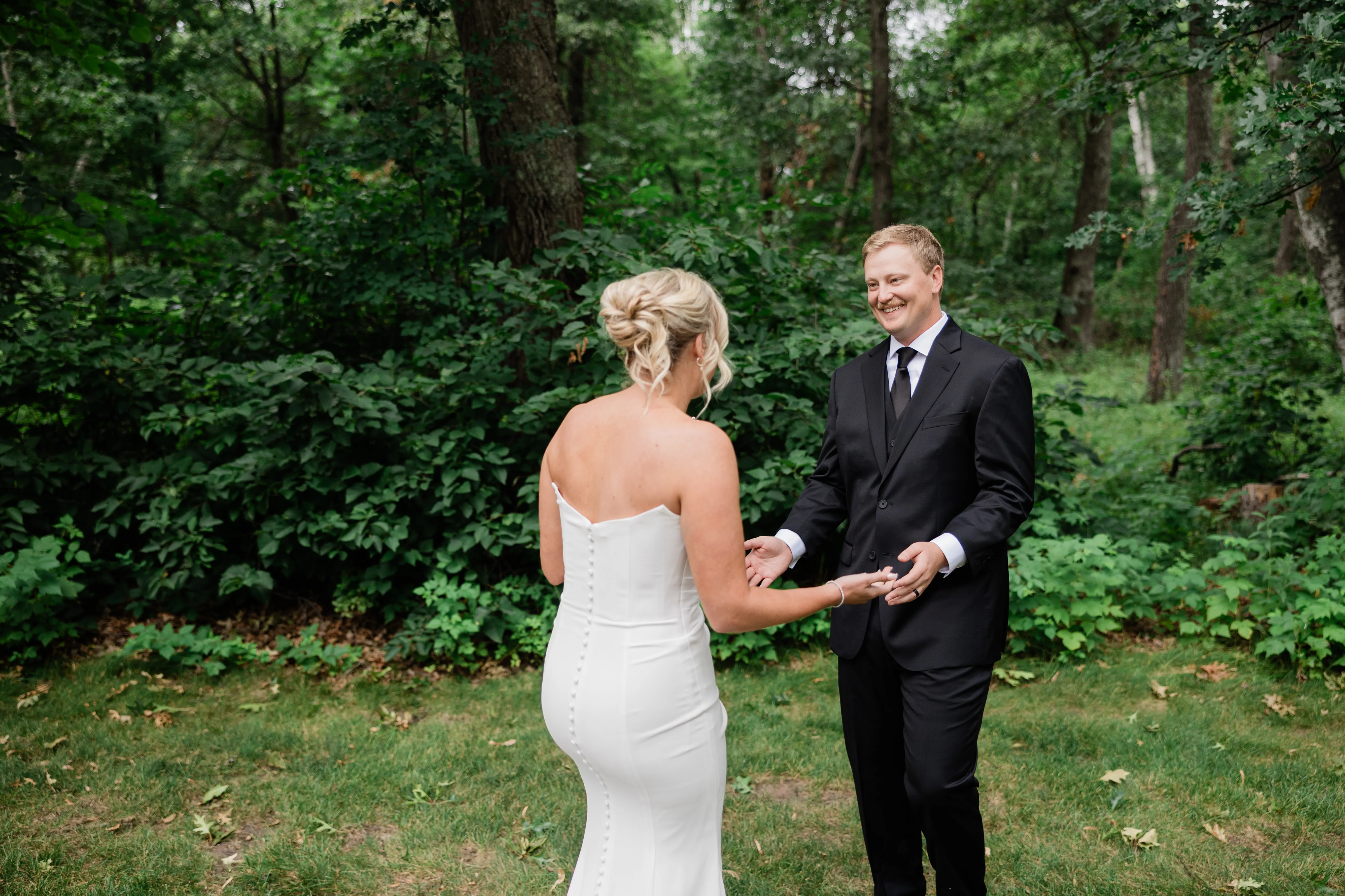Carter turns and grins at Amy during their first look in the woods behind Whitefish Lodge, reaching for her hands — Tim Larsen Photography, Brainerd Lakes MN