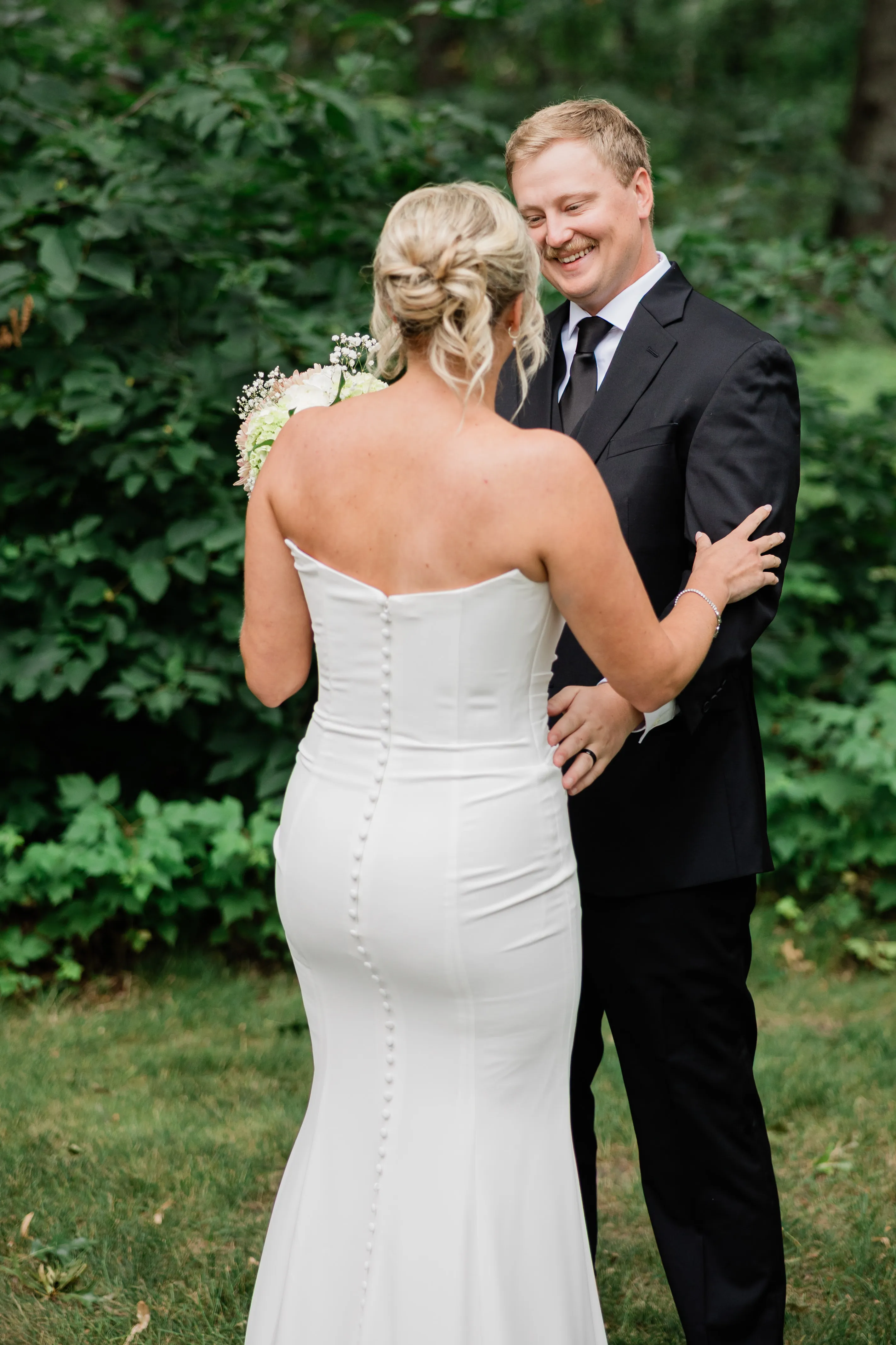 Amy and Carter hold both hands at the edge of the wooded lawn beside the lodge during their first look — Tim Larsen Photography, Brainerd Lakes MN
