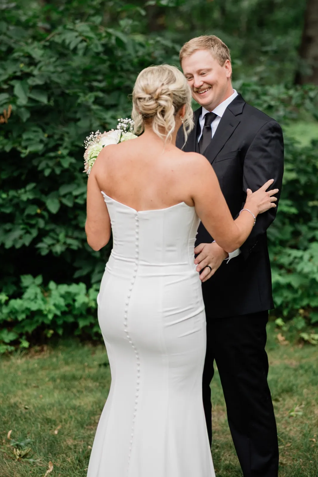 Amy and Carter hold both hands at the edge of the wooded lawn beside the lodge during their first look — Tim Larsen Photography, Brainerd Lakes MN