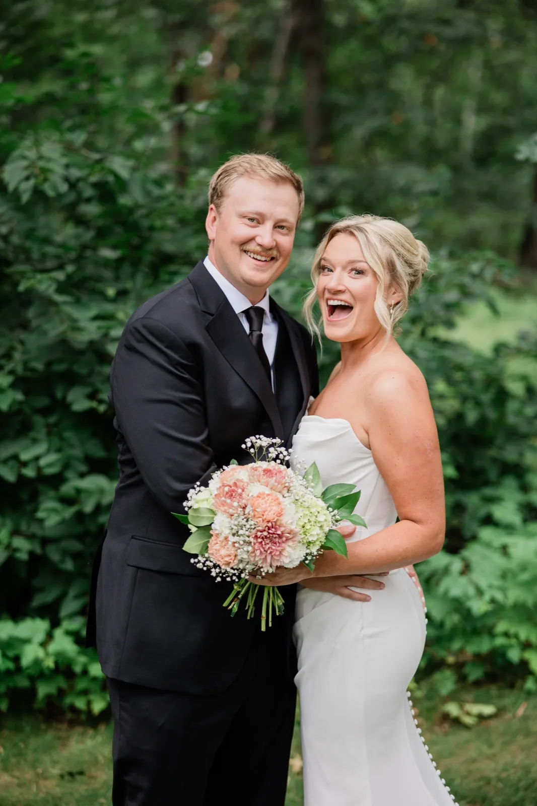 Amy laughs mid-sentence as Carter smiles at the camera, the peach and white bouquet held between them — Tim Larsen Photography, Brainerd Lakes MN