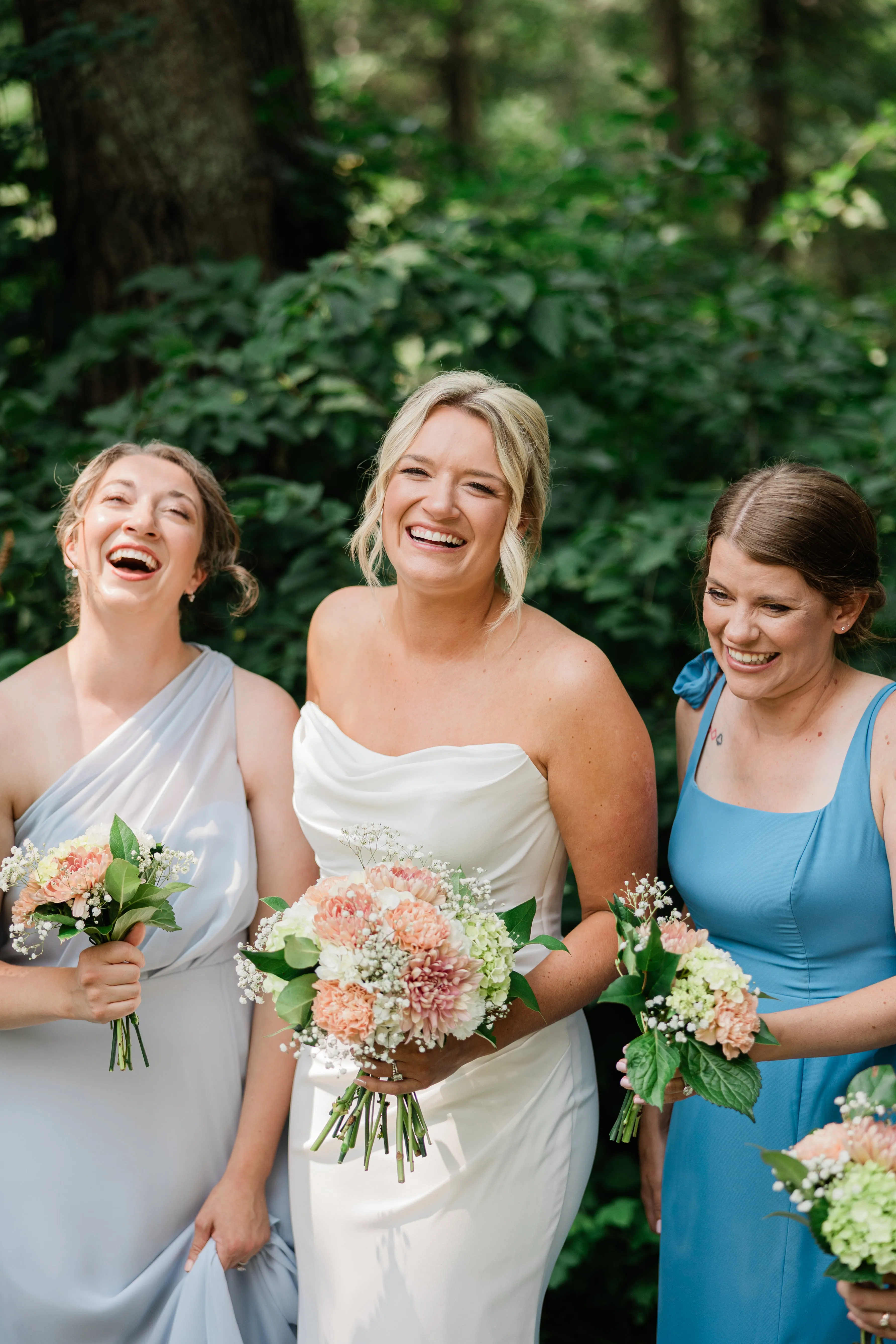 Amy laughs with two attendants in blue dresses, all three holding peach and white bouquets — Tim Larsen Photography, Brainerd Lakes MN