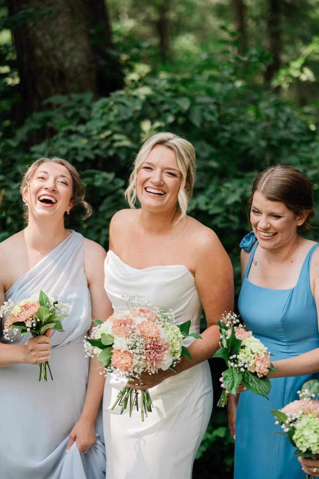 Amy laughs with two attendants in blue dresses, all three holding peach and white bouquets — Tim Larsen Photography, Brainerd Lakes MN