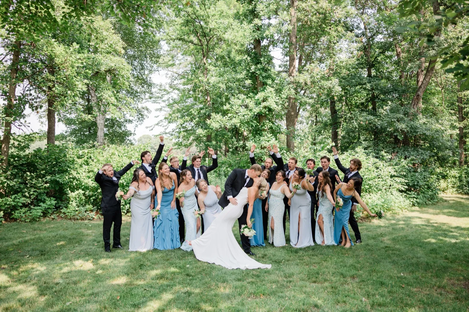 Carter dips Amy for a kiss on the green lawn while their family and friends cheer with raised arms behind them — Tim Larsen Photography, Brainerd Lakes MN