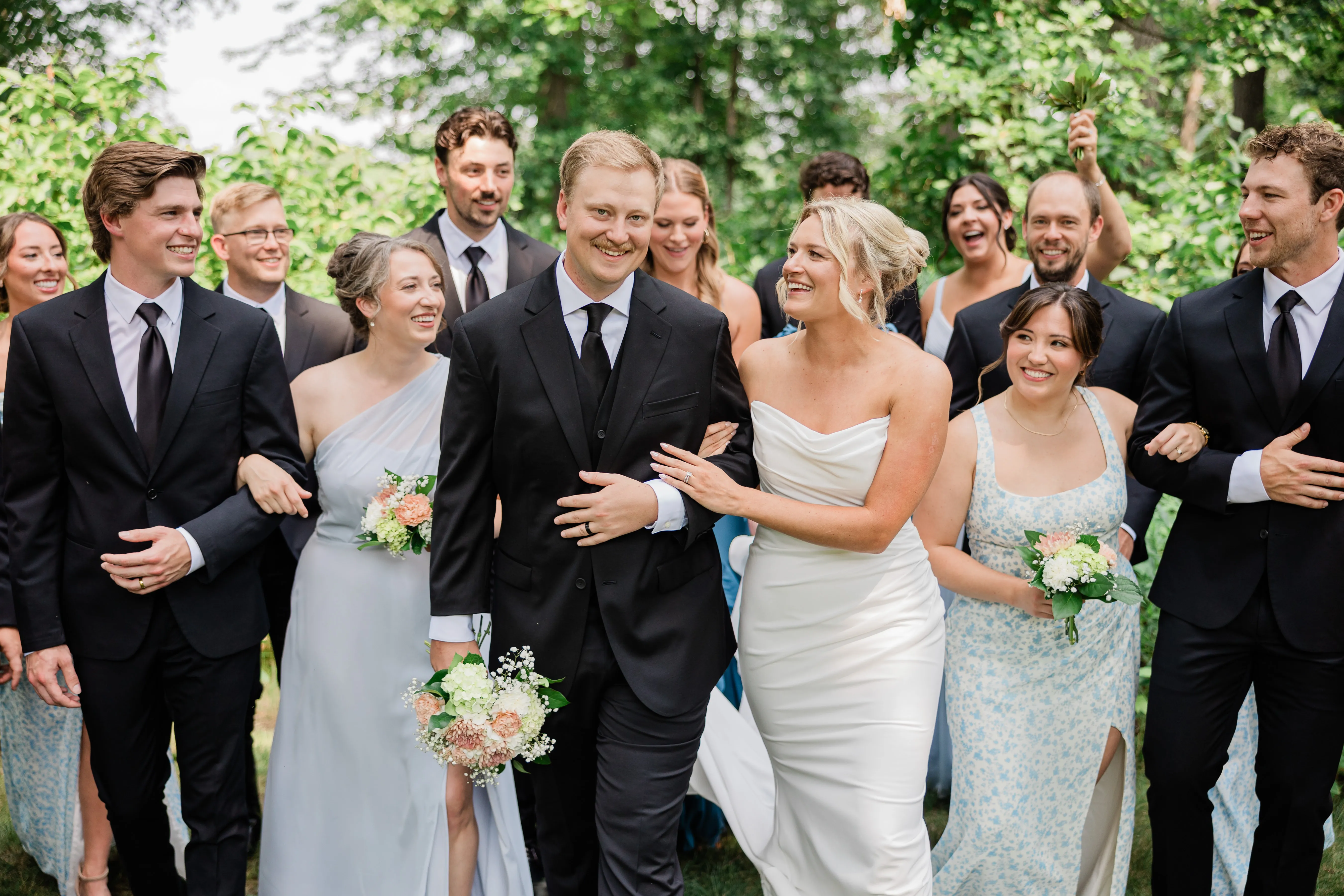 Amy and Carter walk arm in arm at the center of a large group of family and friends beneath a green canopy at Whitefish Lodge — Tim Larsen Photography, Brainerd Lakes MN