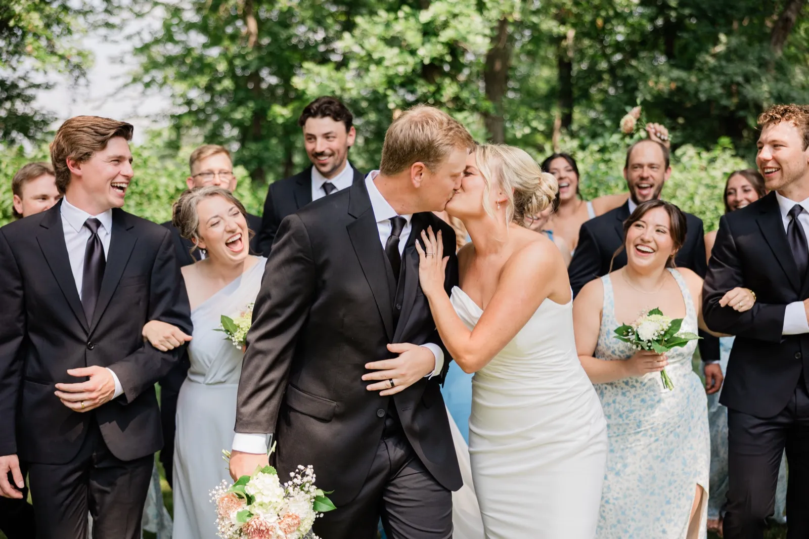Amy and Carter kiss surrounded by their laughing family and friends on the back lawn tree line — Tim Larsen Photography, Brainerd Lakes MN