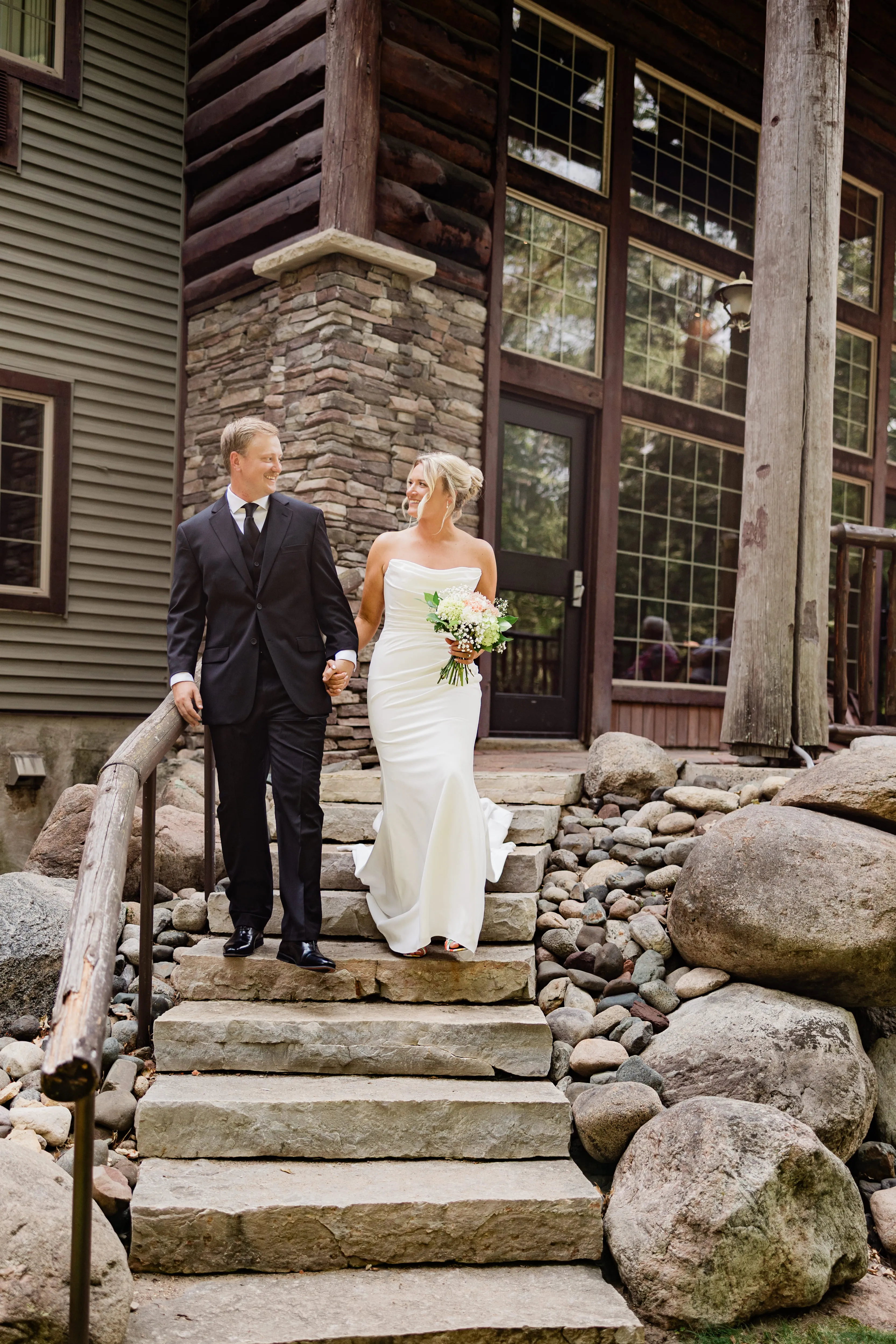 Amy and Carter hold hands walking down the wide stone steps outside the log-and-stone exterior of Whitefish Lodge — Tim Larsen Photography, Brainerd Lakes MN
