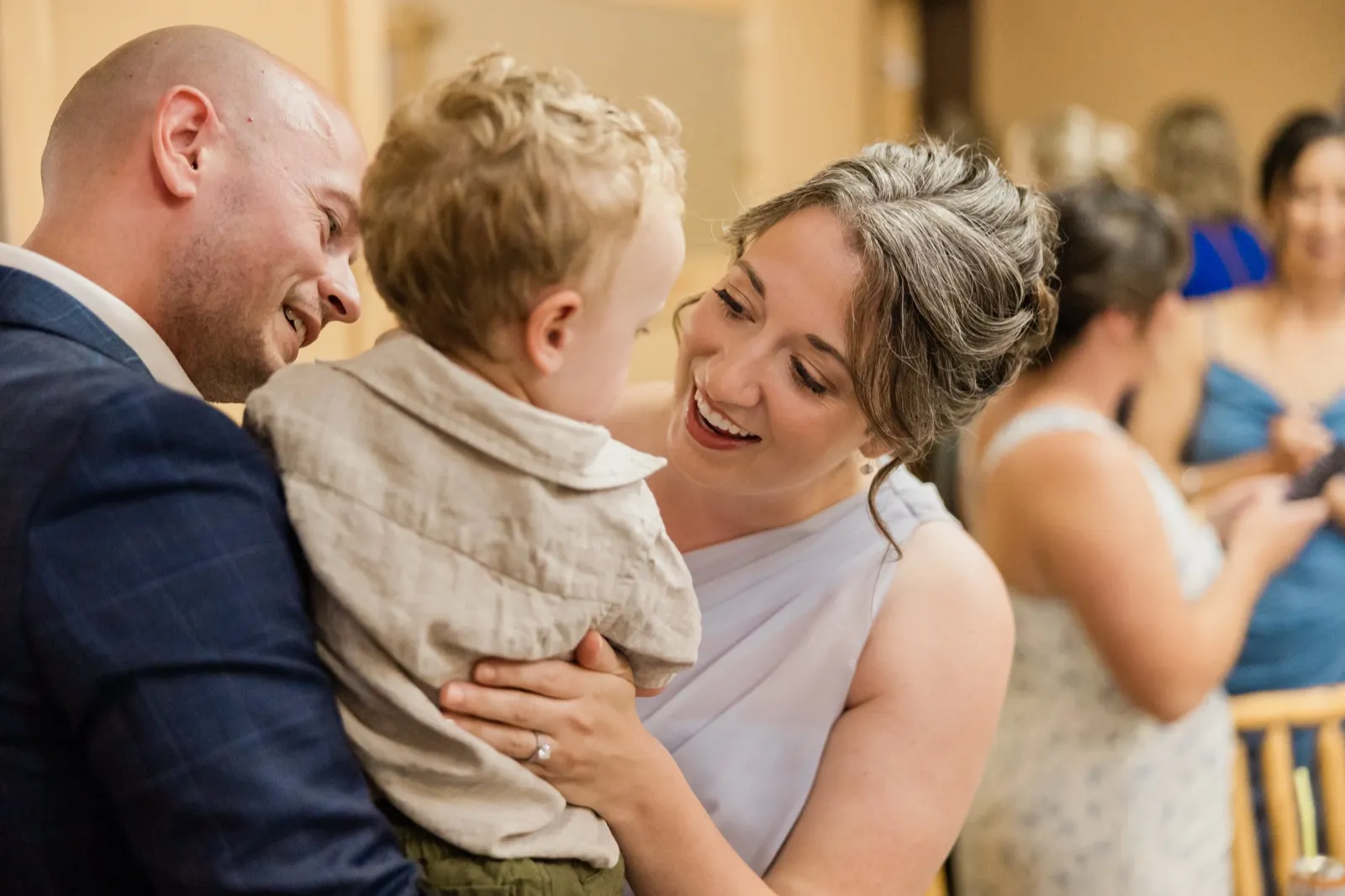 A guest in a lavender dress laughs at a toddler held by a man in a navy suit inside the lodge — Tim Larsen Photography, Brainerd Lakes MN