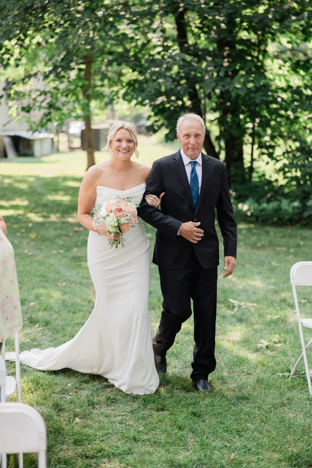 Amy walks the grass aisle on the arm of the man who gave her away, holding a blush and white bouquet — Tim Larsen Photography, Brainerd Lakes MN