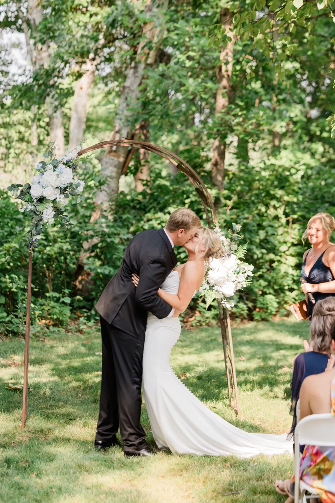 Carter dips Amy into a kiss beneath the circular floral arch as their officiant smiles nearby — Tim Larsen Photography, Brainerd Lakes MN