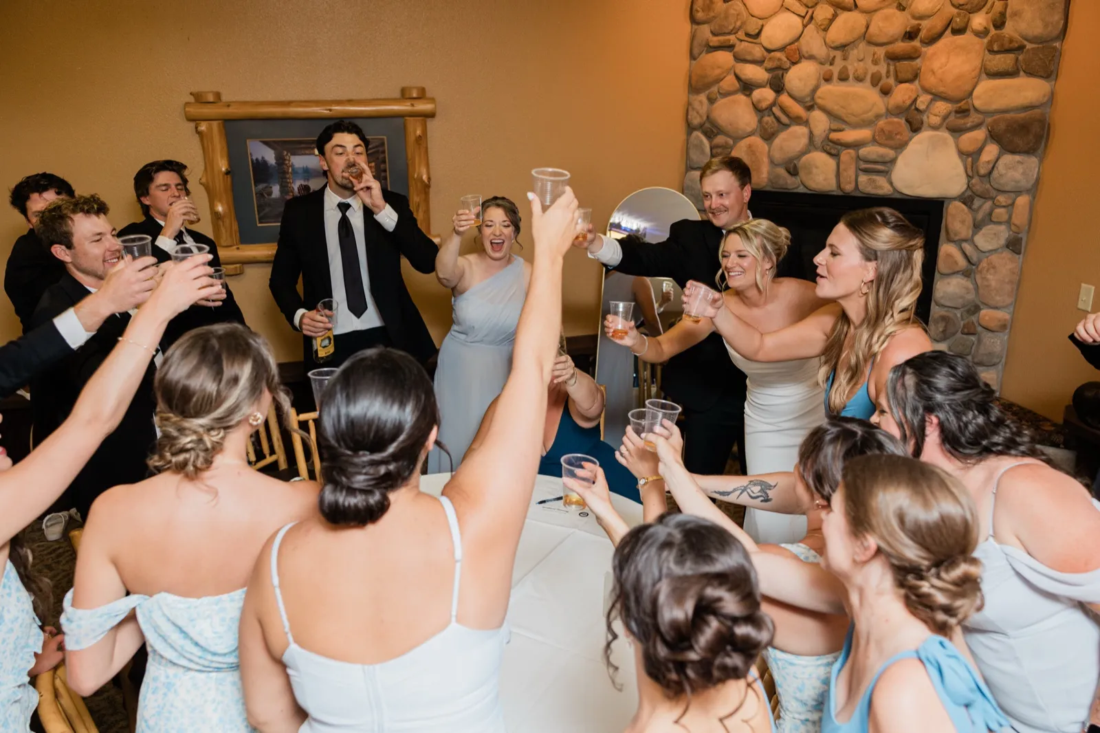 Everyone raises plastic cups in a toast around Amy and Carter beside the river-rock fireplace inside Whitefish Lodge — Tim Larsen Photography, Brainerd Lakes MN