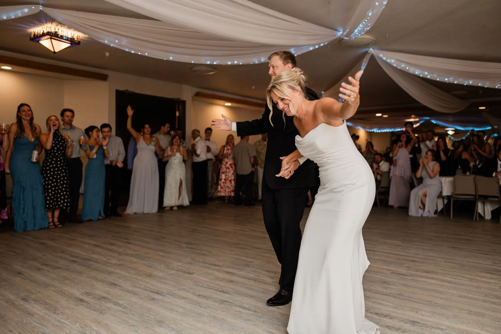 Amy and Carter throw their arms wide mid-first-dance as guests ring the floor at Whitefish Lodge — Tim Larsen Photography, Brainerd Lakes MN