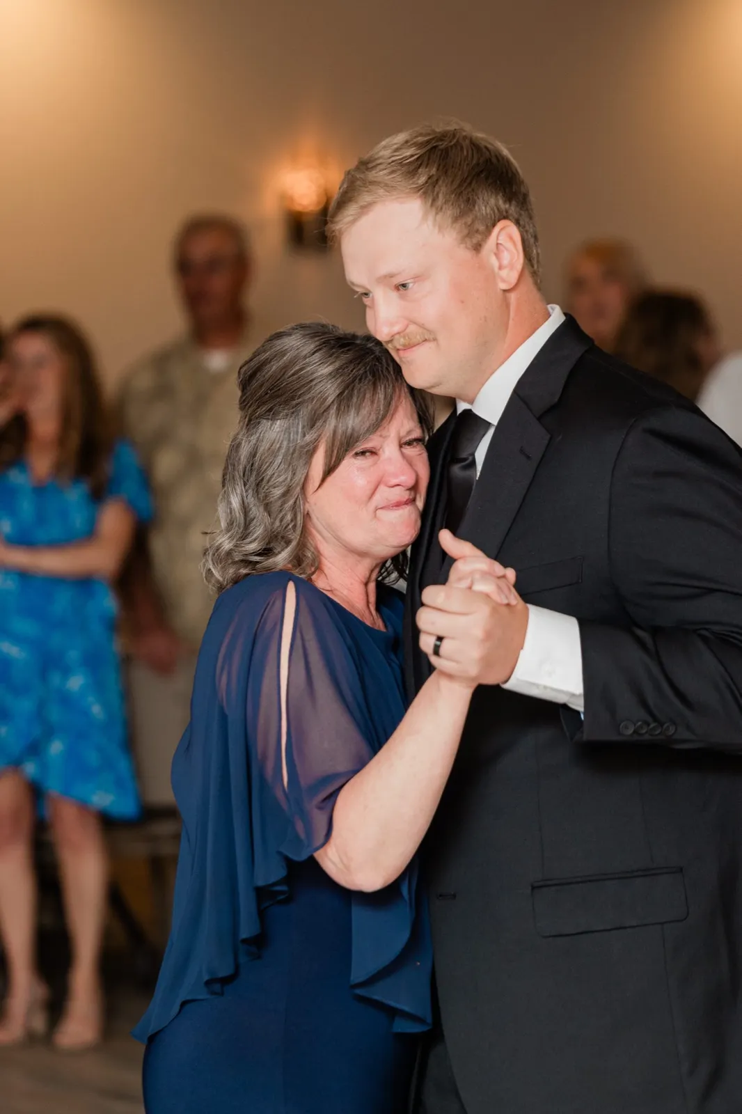 Carter dances with his mother, her head against his shoulder and tears in her eyes, guests watching from the floor's edge — Tim Larsen Photography, Brainerd Lakes MN