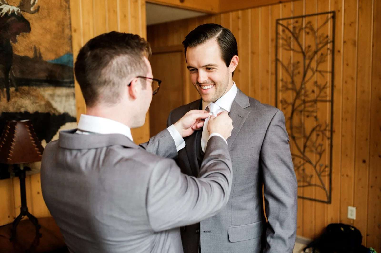 A groomsman adjusts the groom's tie as the groom laughs in a wood-paneled cabin room at Grand View Lodge. — Tim Larsen Photography, Brainerd Lakes MN