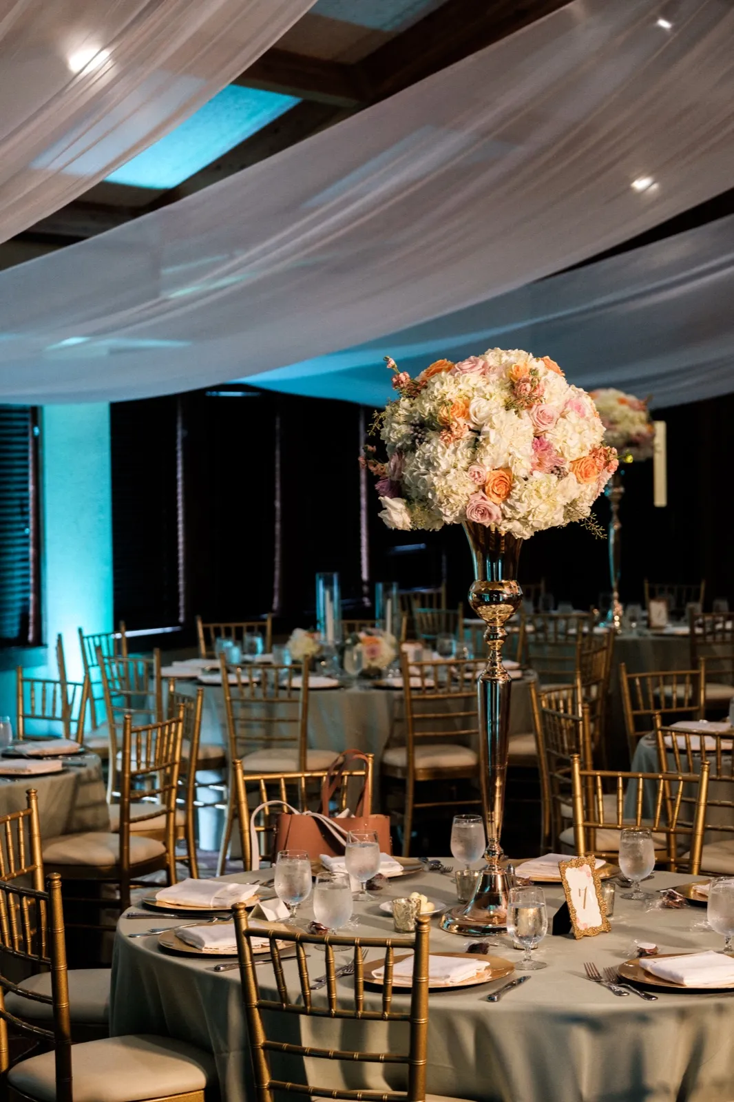 A tall pastel floral centerpiece rises above a set reception table at Grand View Lodge, with draped fabric and teal uplighting overhead in the ballroom. — Tim Larsen Photography, Brainerd Lakes MN