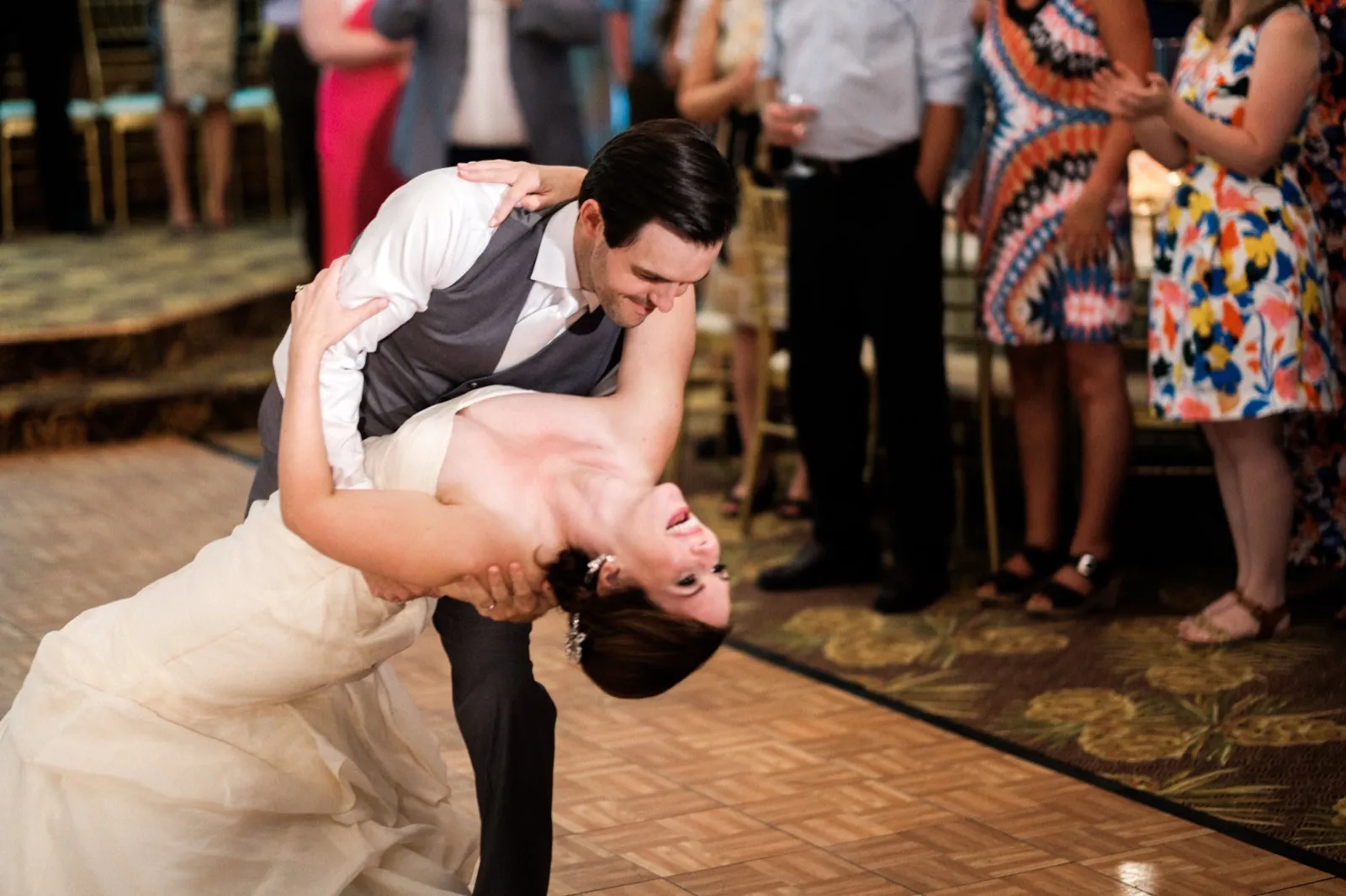 The groom dips the bride at the end of their first dance as she laughs, surrounded by guests watching from the edge of the ballroom floor. — Tim Larsen Photography, Brainerd Lakes MN