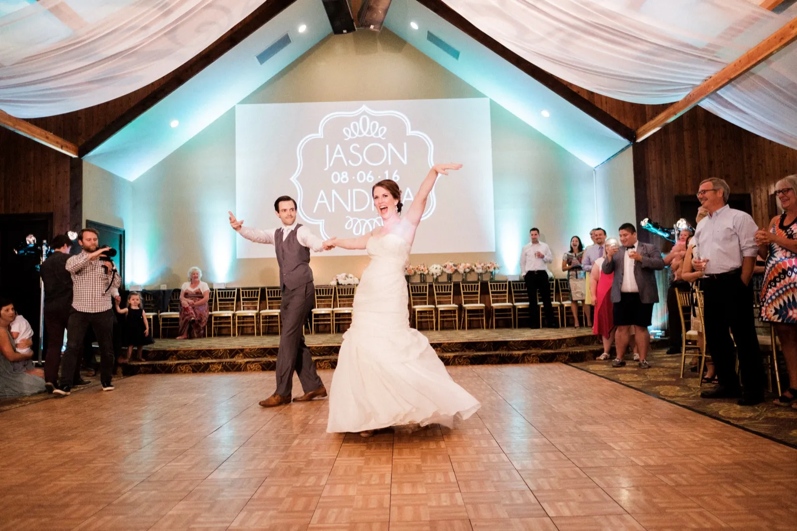 The bride throws her arm in the air mid-twirl as the groom guides her across the ballroom dance floor beneath a custom monogram projection and draped peaked ceiling. — Tim Larsen Photography, Brainerd Lakes MN