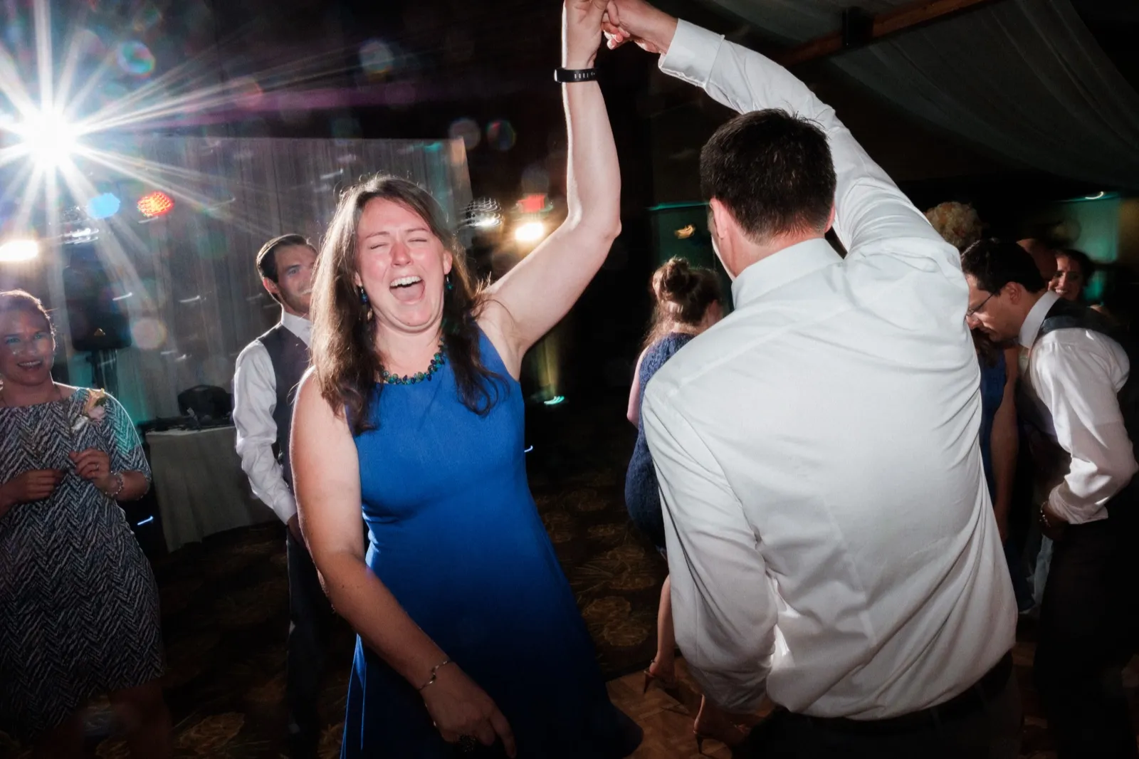 A guest in a blue dress laughs with her eyes closed as a partner spins her under a starburst stage light on the reception dance floor. — Tim Larsen Photography, Brainerd Lakes MN