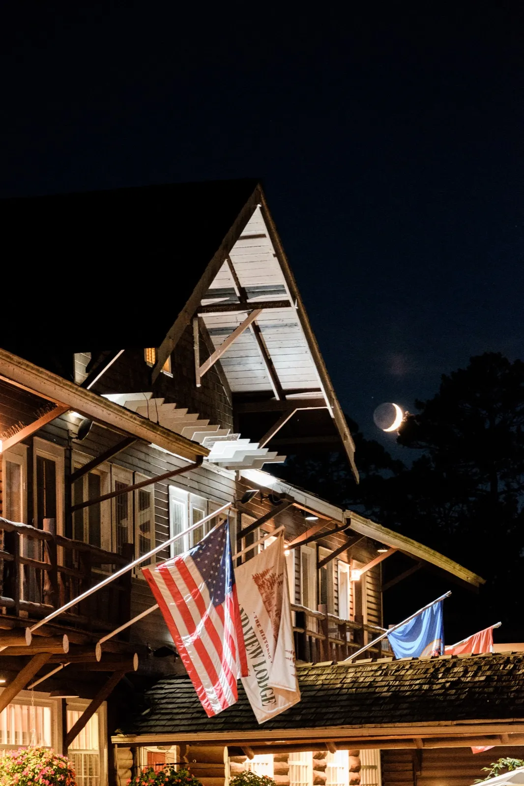 The peaked roofline of Grand View Lodge at night with American flag and Grand View Lodge banner hanging beneath a crescent moon. — Tim Larsen Photography, Brainerd Lakes MN