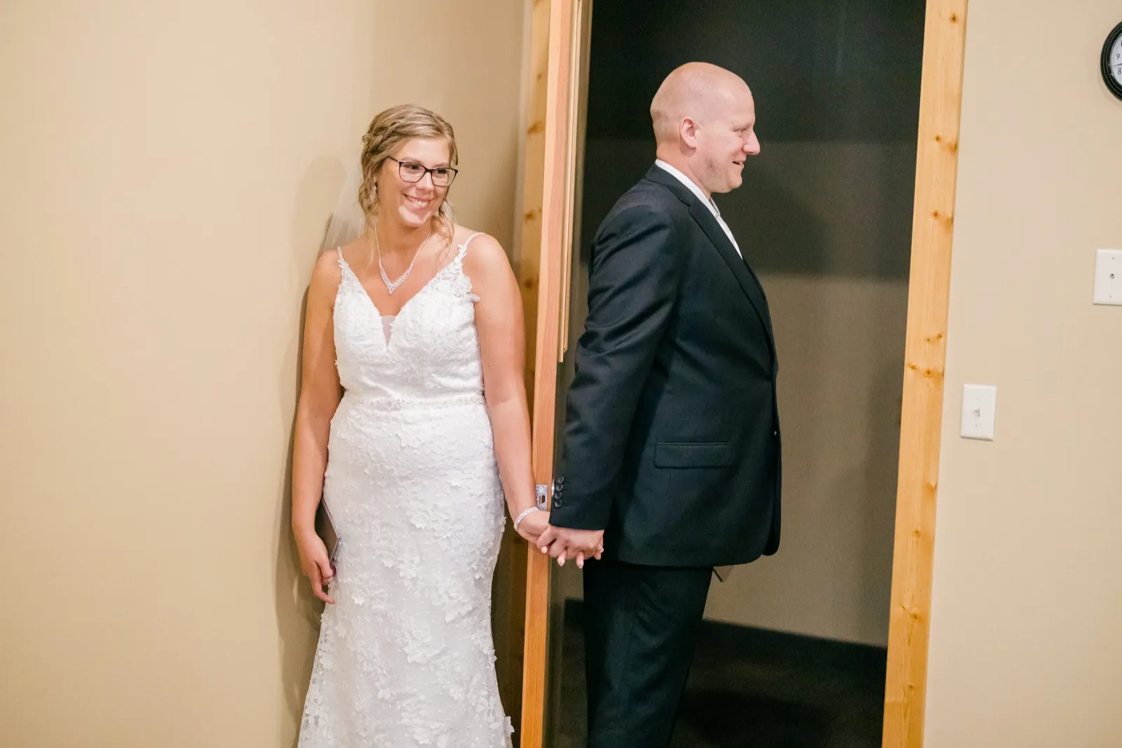 Kim smiles widely while holding hands with Jesse around a doorframe that separates them before their first look — Tim Larsen Photography, Brainerd Lakes MN