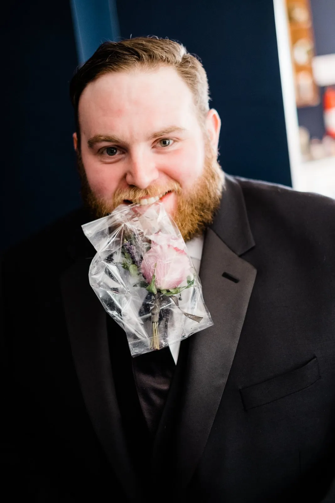 Playful pre-ceremony portrait — groom grins while holding his bagged boutonniere between his teeth, Duluth Catholic spring wedding getting-ready — Tim Larsen Photography, Duluth MN