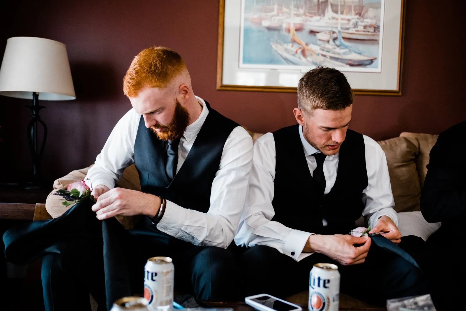 Groomsmen pin boutonnieres in the warm getting-ready suite, framed by a lamp and nautical painting — Duluth spring wedding — Tim Larsen Photography, Duluth MN