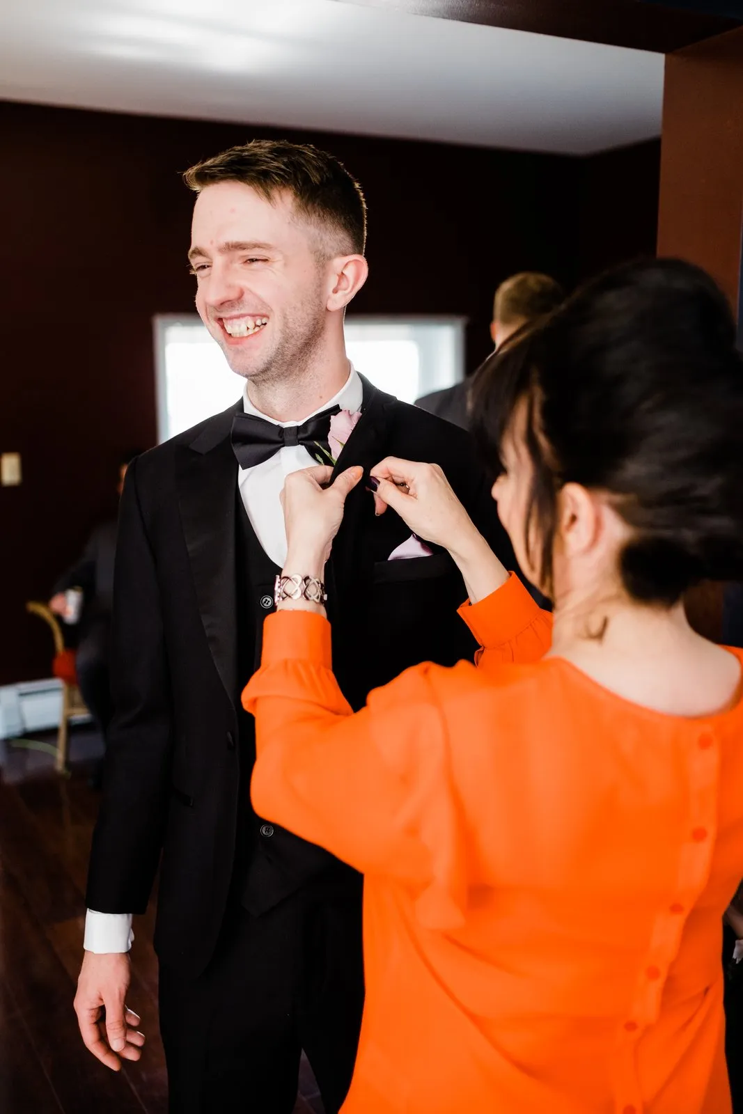 Groom laughs as his mother pins his boutonniere in warm window light — Duluth Catholic spring wedding getting-ready — Tim Larsen Photography, Duluth MN