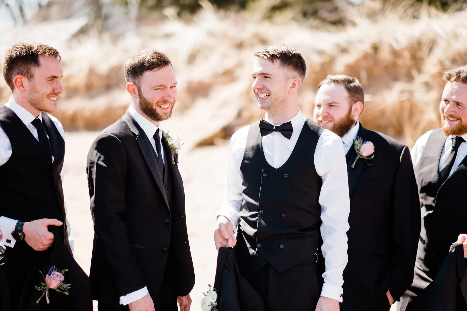 Groomsmen in a row mid-laugh, golden Lake Superior dune grass softly blurred behind — Duluth Catholic spring wedding — Tim Larsen Photography, Duluth MN