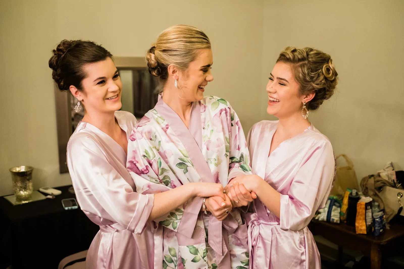 Bride centered in a floral robe between bridesmaids mid-laugh — Greysolon Plaza bridal suite, Duluth Catholic spring wedding — Tim Larsen Photography, Duluth MN