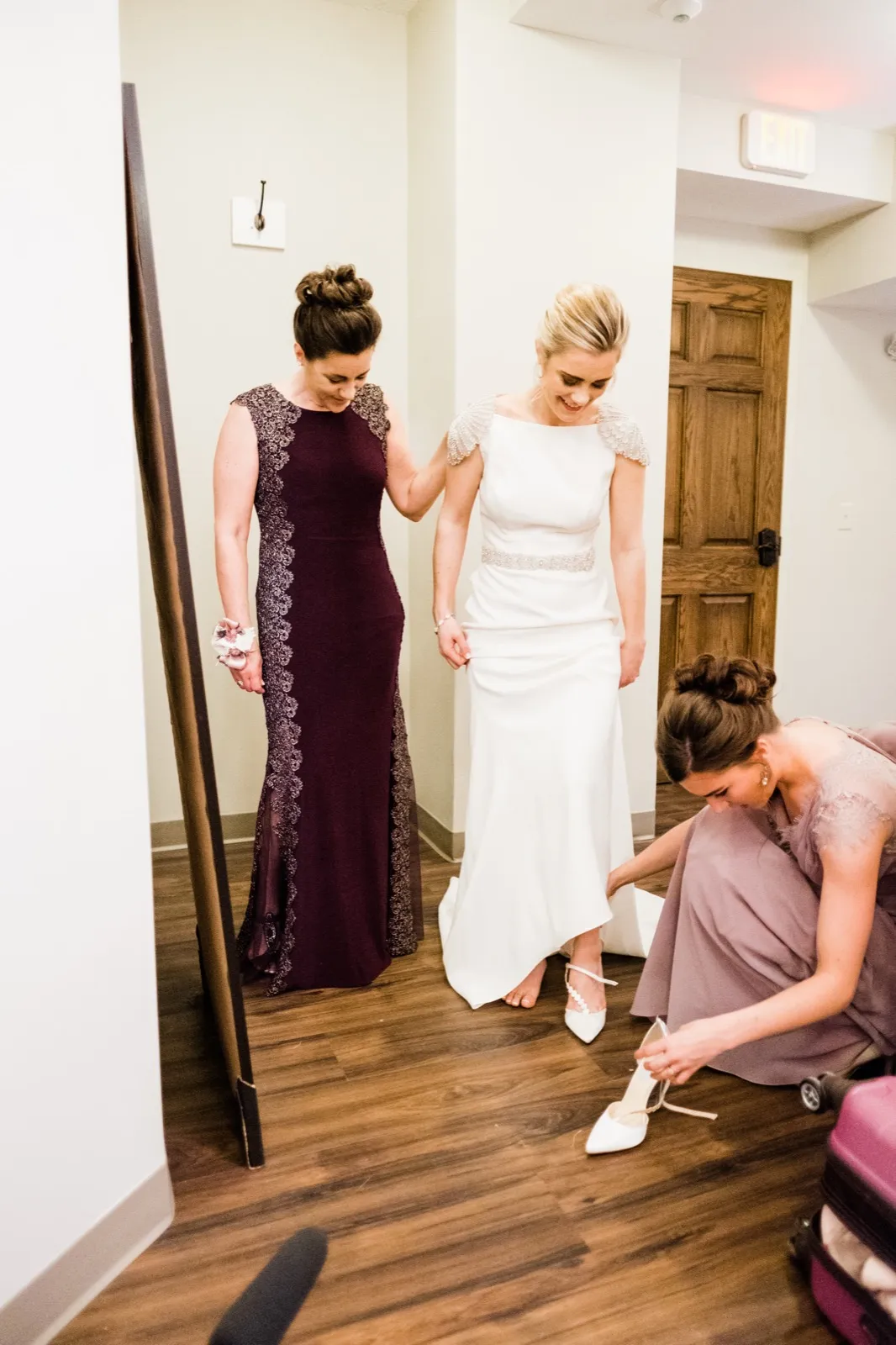 Bride flanked by her mother as a bridesmaid kneels with her shoes — Greysolon Plaza bridal suite, Duluth Catholic spring wedding — Tim Larsen Photography, Duluth MN