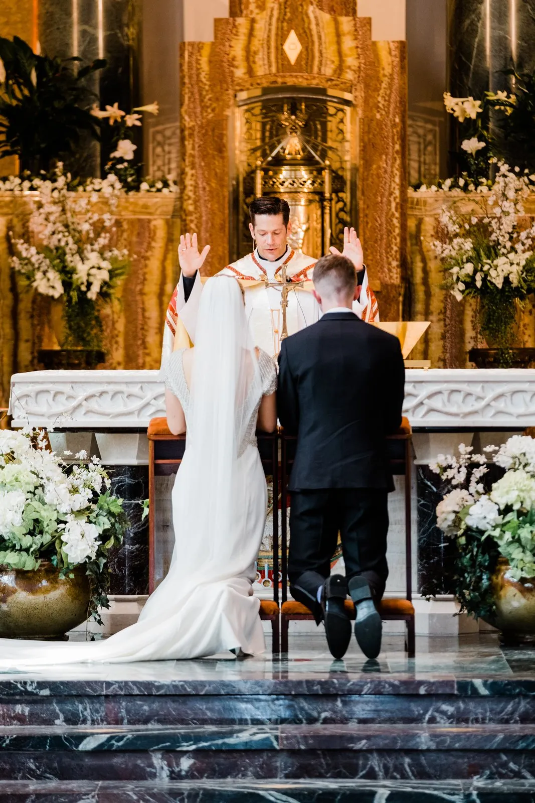 Priest's raised hands above the kneeling couple at the altar, bride's veil trailing — Catholic ceremony at the Cathedral of Our Lady of the Rosary — Tim Larsen Photography, Duluth MN