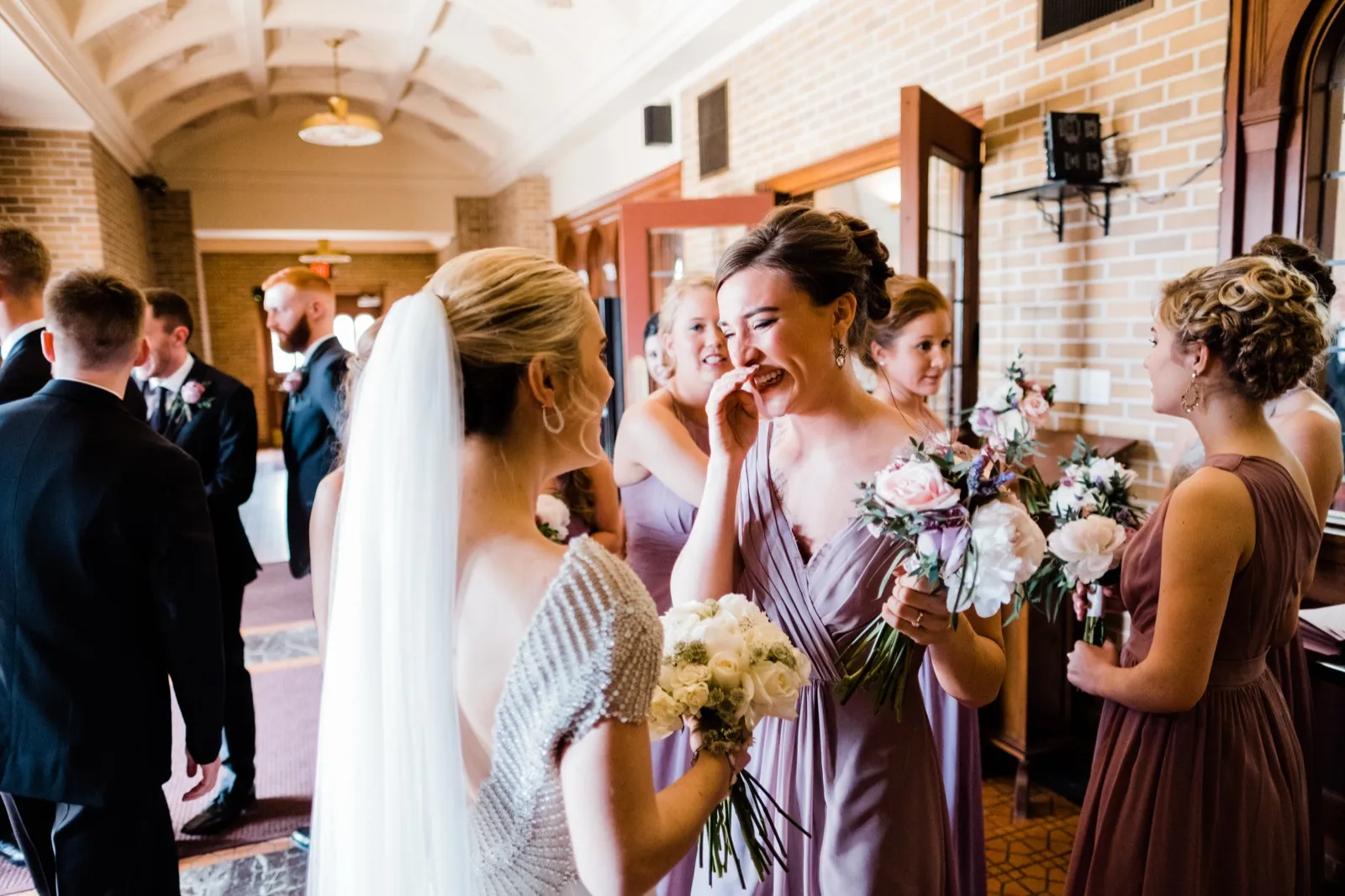 Bride and a dusty-mauve bridesmaid share laughter in the warm vaulted brick hallway after the ceremony — Cathedral of Our Lady of the Rosary, Duluth — Tim Larsen Photography, Duluth MN