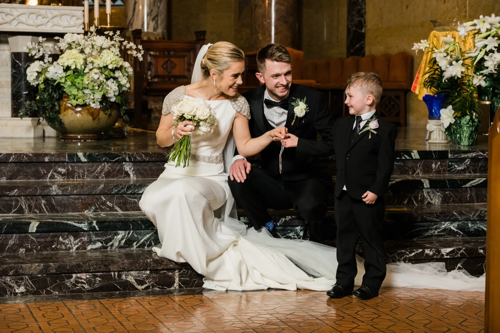 Couple seated on the marble altar steps engaging the young ring bearer between floral arrangements — Cathedral of Our Lady of the Rosary — Tim Larsen Photography, Duluth MN