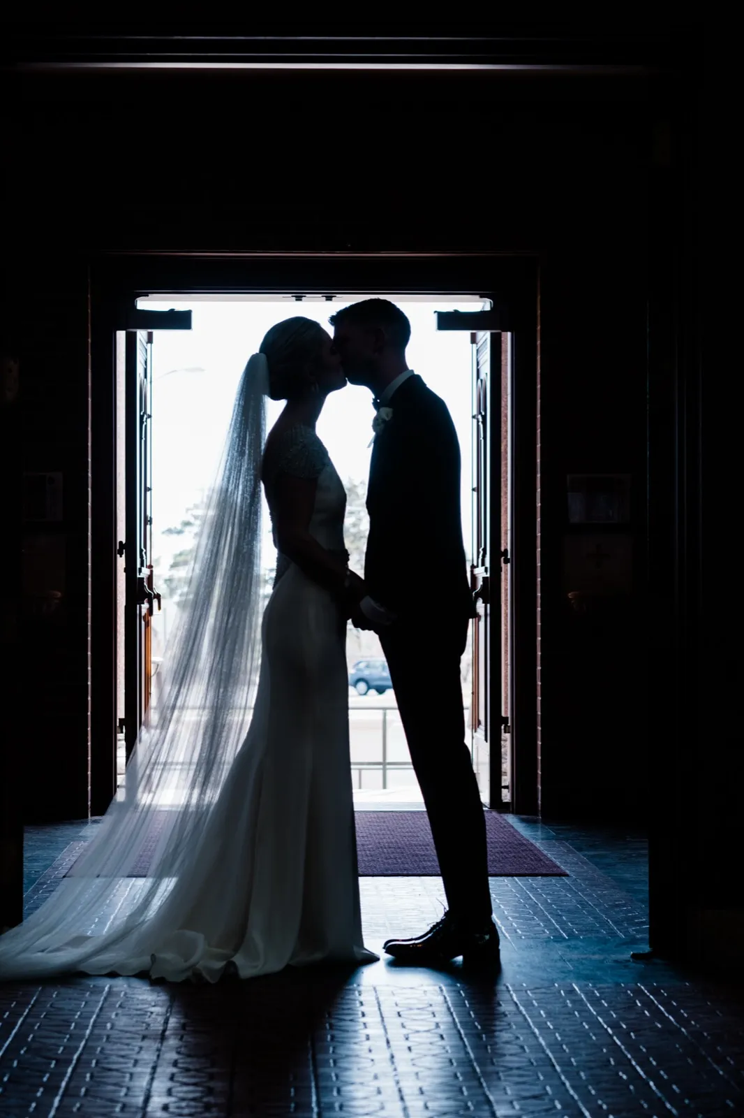 Centered silhouette of the couple in the Cathedral doorway, veil cascading across the tiled floor — strong backlit Cathedral of Our Lady of the Rosary exit — Tim Larsen Photography, Duluth MN