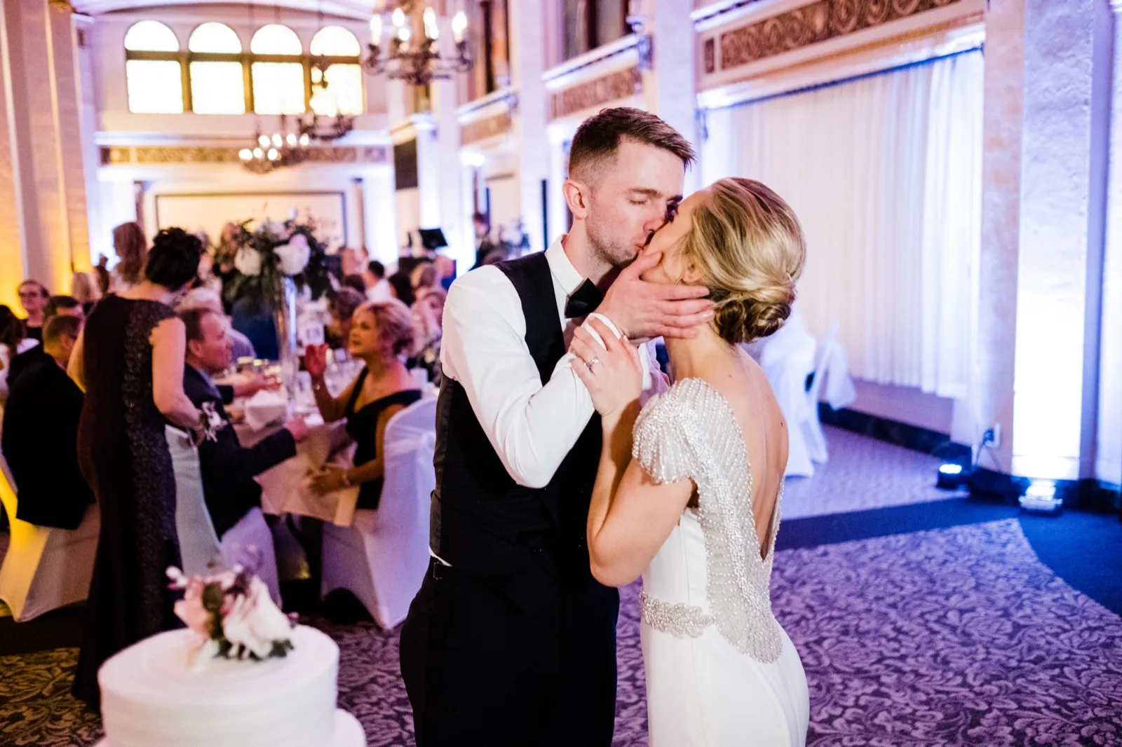 Couple kiss right of frame with the cake foreground left, ornate ballroom architecture behind — Greysolon Ballroom cake cutting, Duluth wedding — Tim Larsen Photography, Duluth MN