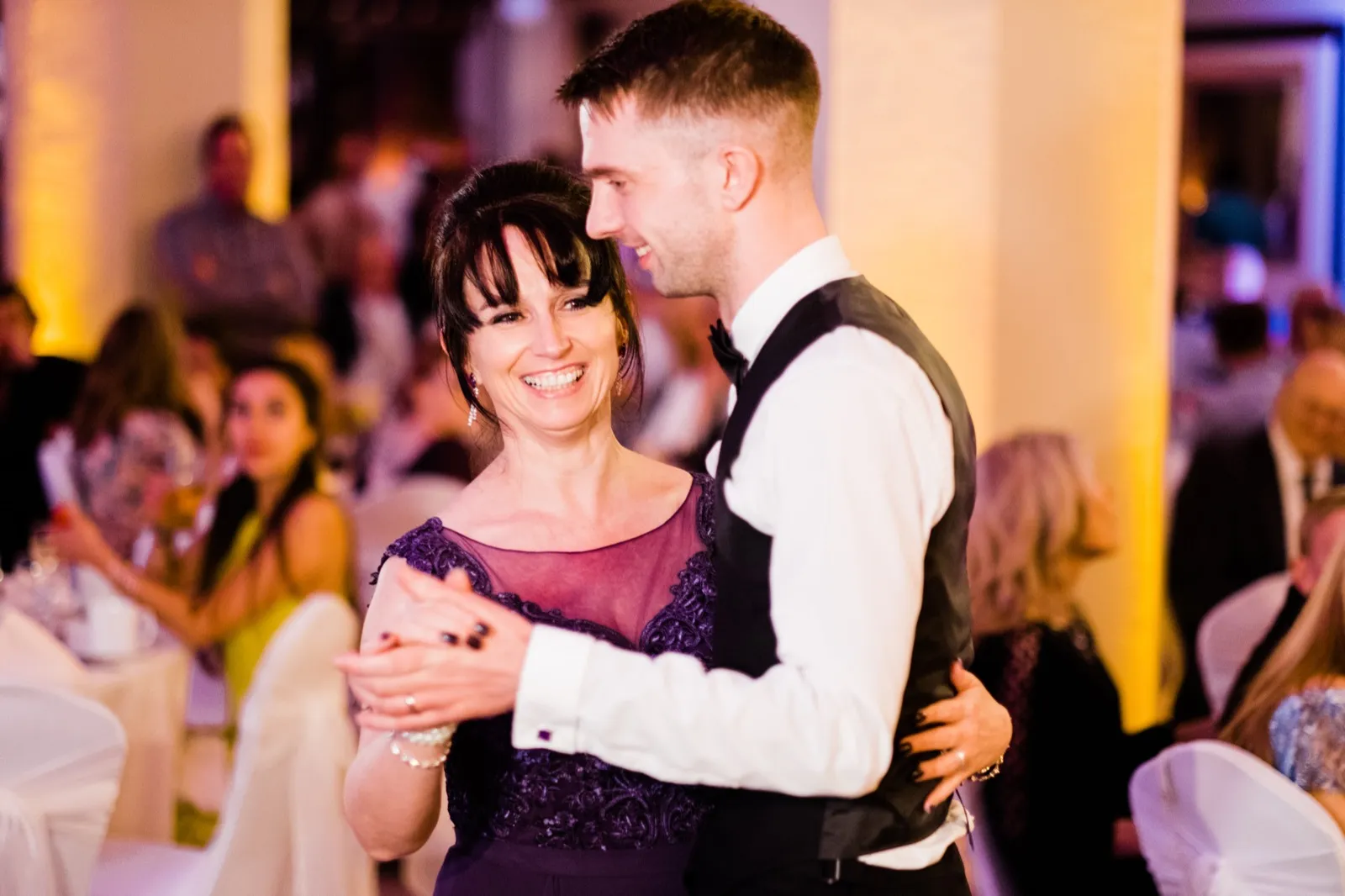 Mother beams over the groom's shoulder during their dance, warm uplighting on the columns behind — Greysolon Ballroom, Duluth Catholic wedding — Tim Larsen Photography, Duluth MN