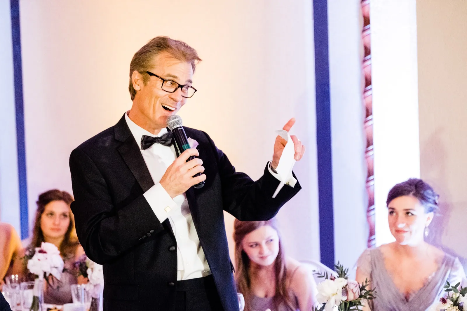 Animated speaker mid-gesture, pointing while holding notes during reception toasts — Greysolon Ballroom, Duluth Catholic spring wedding — Tim Larsen Photography, Duluth MN