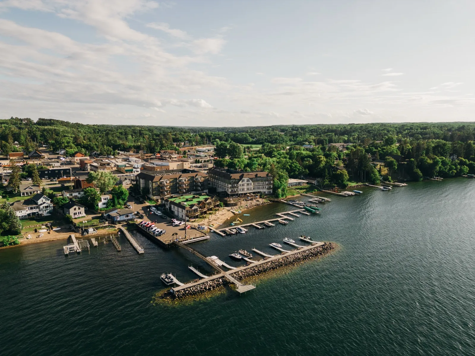 Aerial view of Chase on the Lake resort and its long T-shaped marina dock extending into a calm lake at golden hour, with the small town of Walker visible behind the resort. — Tim Larsen Photography, Brainerd Lakes MN