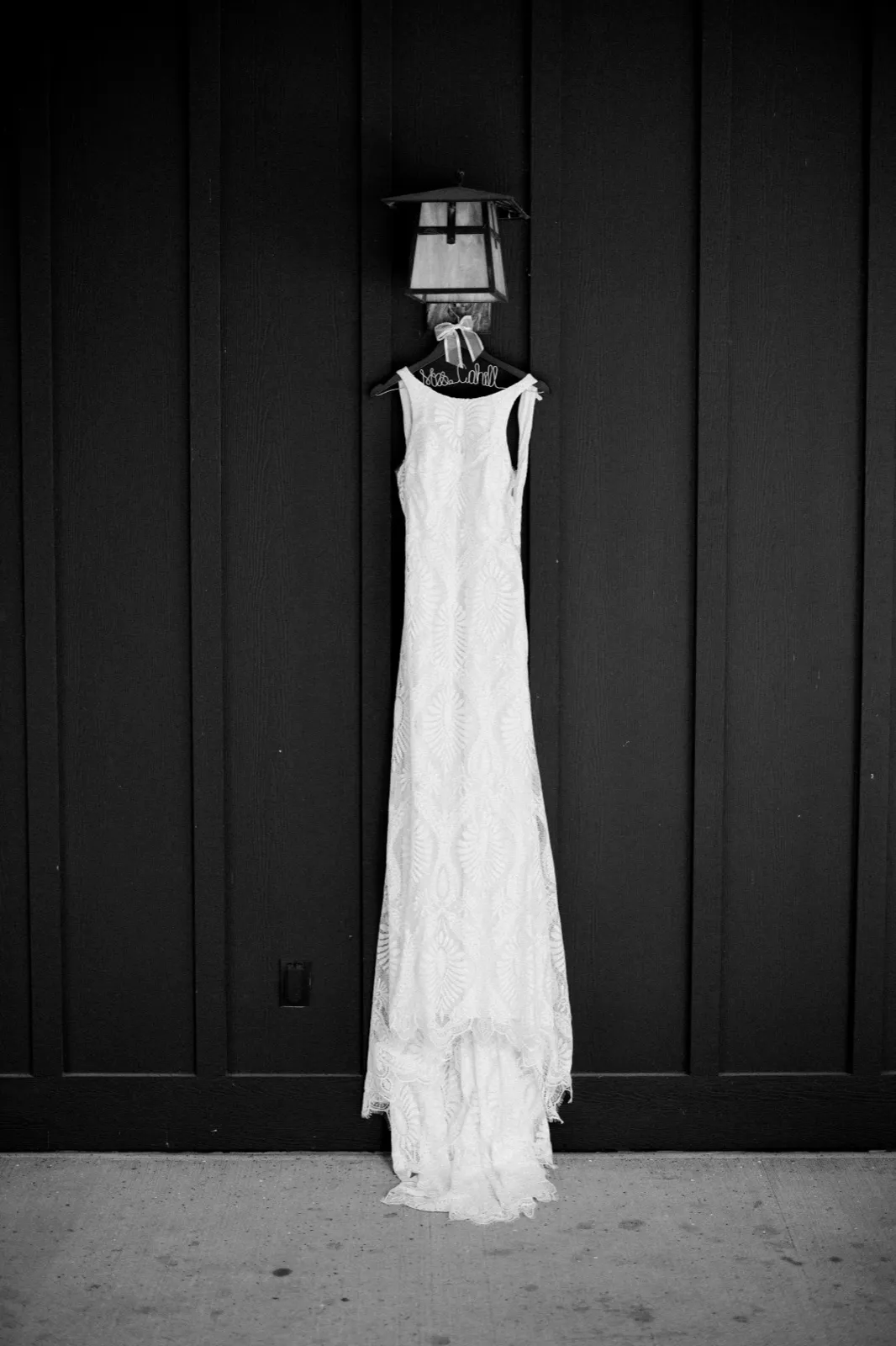 A lace wedding gown hangs from a personalized wire hanger beneath a craftsman lantern on a dark board-and-batten wall at Grand View Lodge. — Tim Larsen Photography, Brainerd Lakes MN
