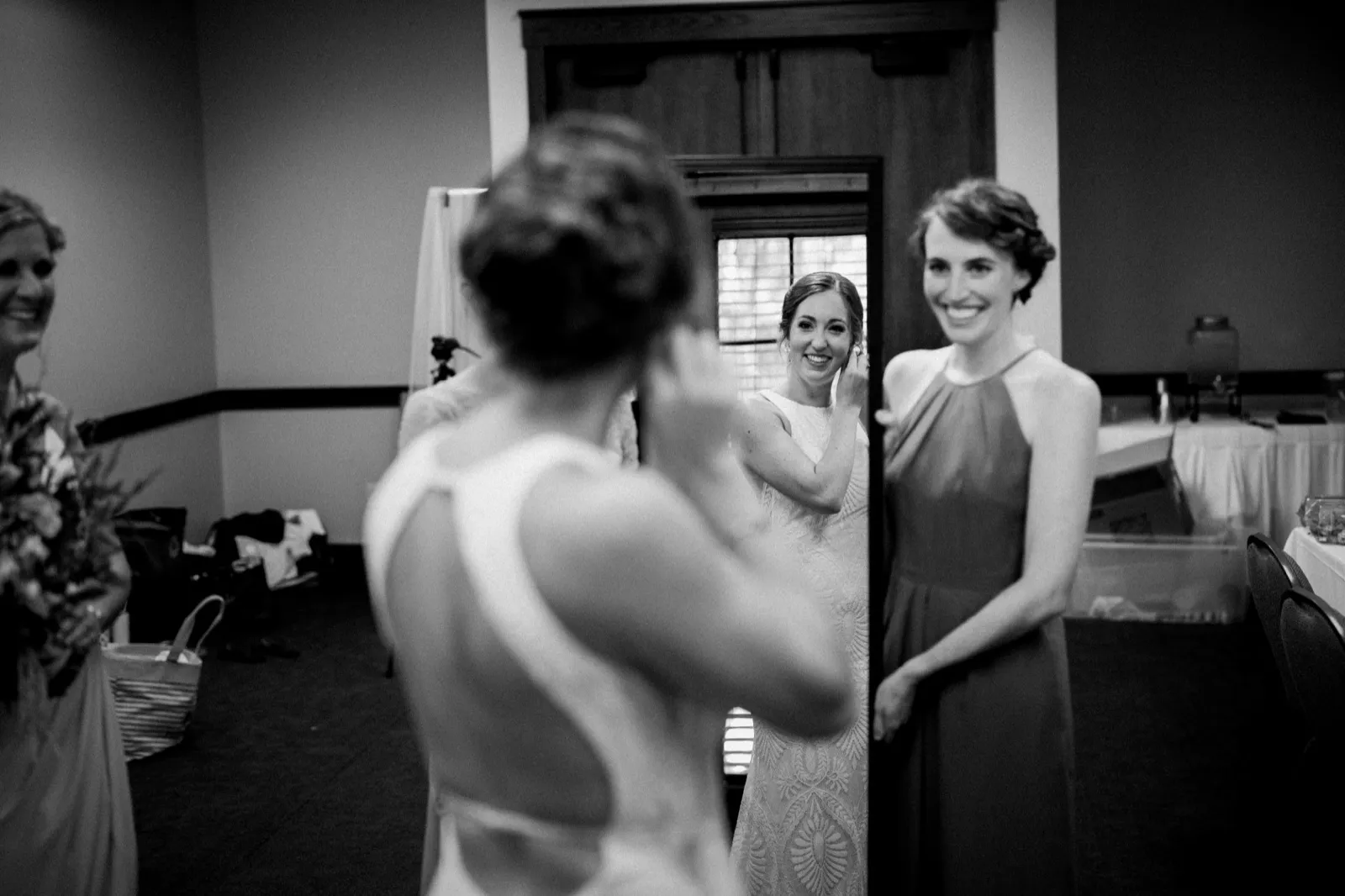 In black and white, bridesmaids stand in a doorway laughing as the out-of-focus bride faces them in the foreground. — Tim Larsen Photography, Brainerd Lakes MN