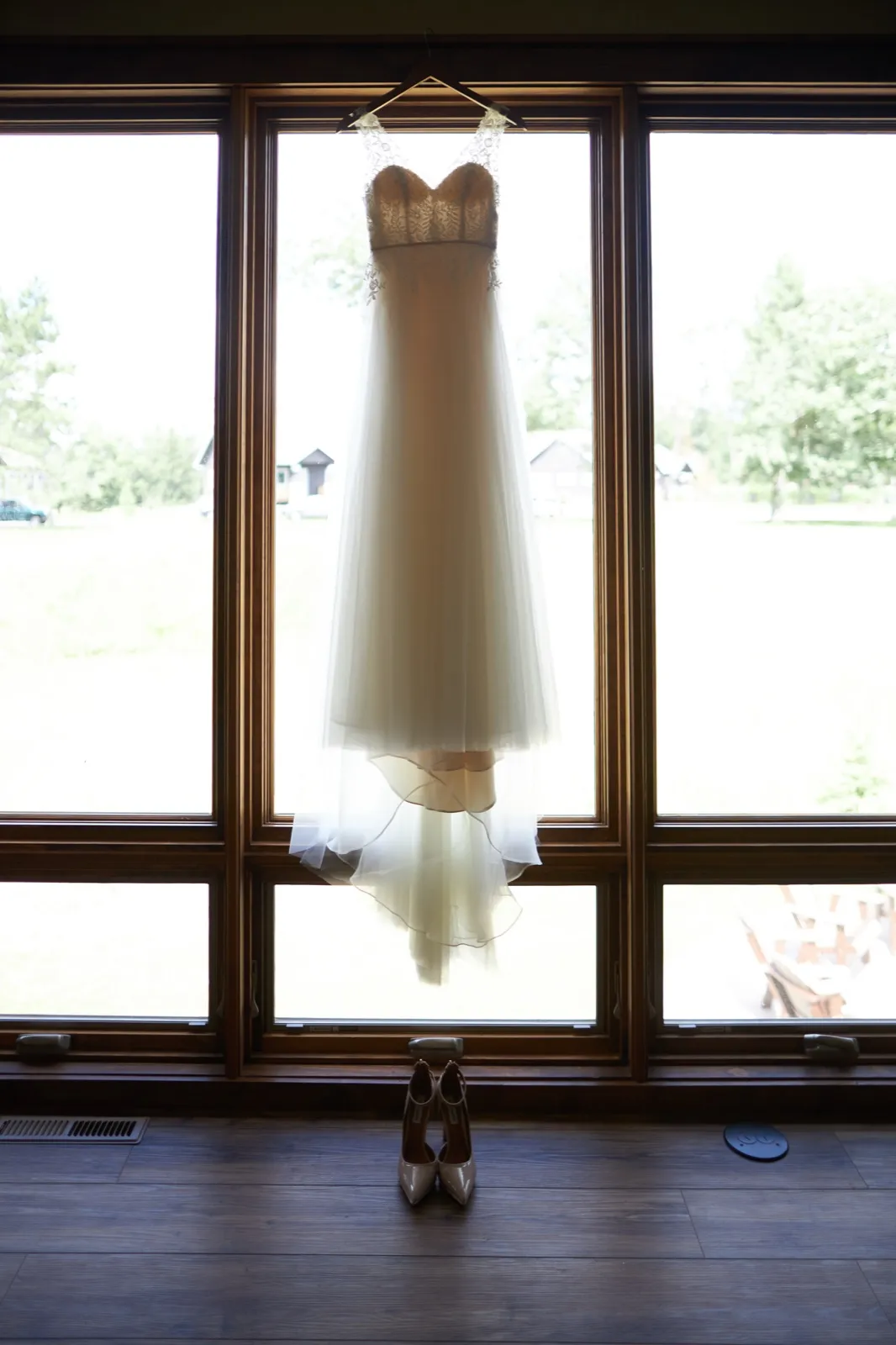 A wedding gown hangs backlit in a tall paneled window with the bride's heels placed on the floor below. — Tim Larsen Photography, Brainerd Lakes MN