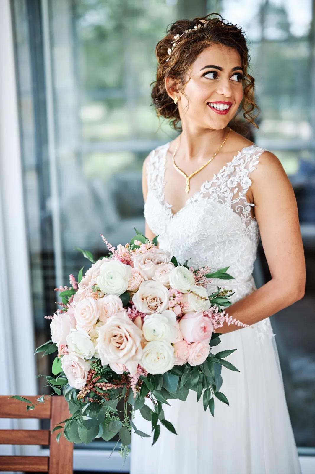The bride smiles and looks off-camera while holding a lush blush and ivory bouquet in soft window light. — Tim Larsen Photography, Brainerd Lakes MN