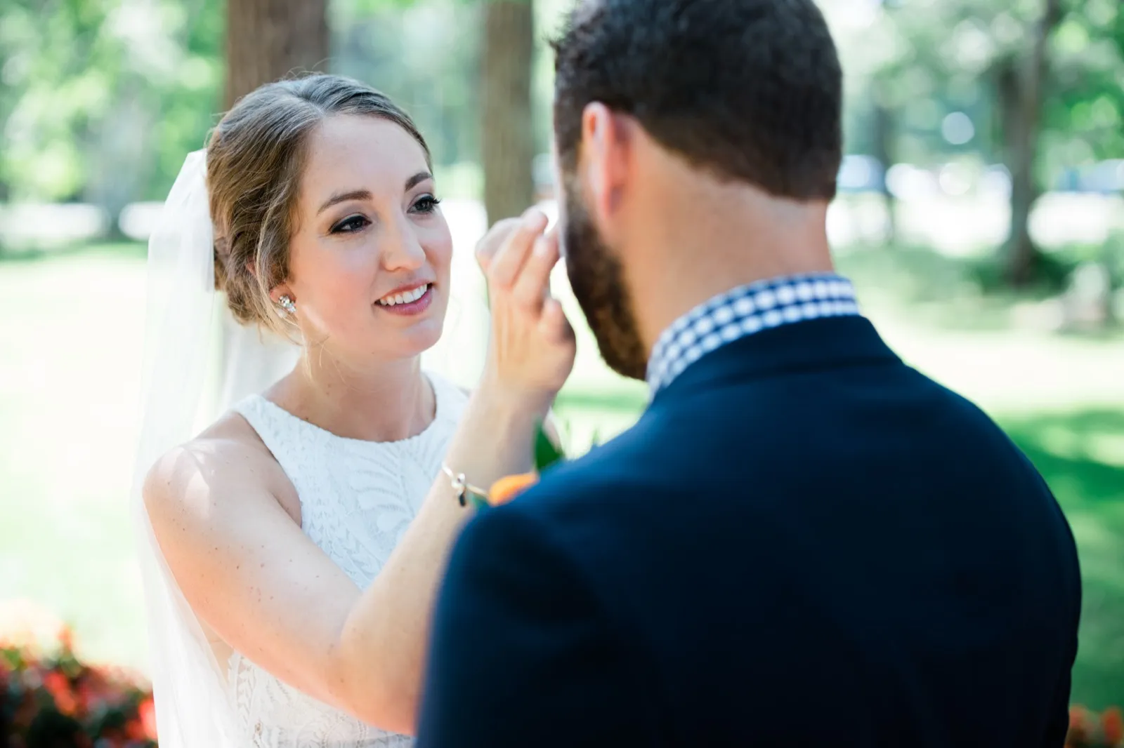 The bride smiles up at the groom as he gently reaches toward her face during their outdoor ceremony beneath tall trees. — Tim Larsen Photography, Brainerd Lakes MN