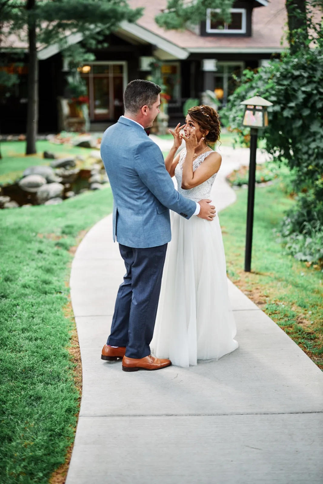 The bride wipes a tear from her eye while the groom holds her waist on a curved walkway in front of the Grand View Lodge entrance. — Tim Larsen Photography, Brainerd Lakes MN