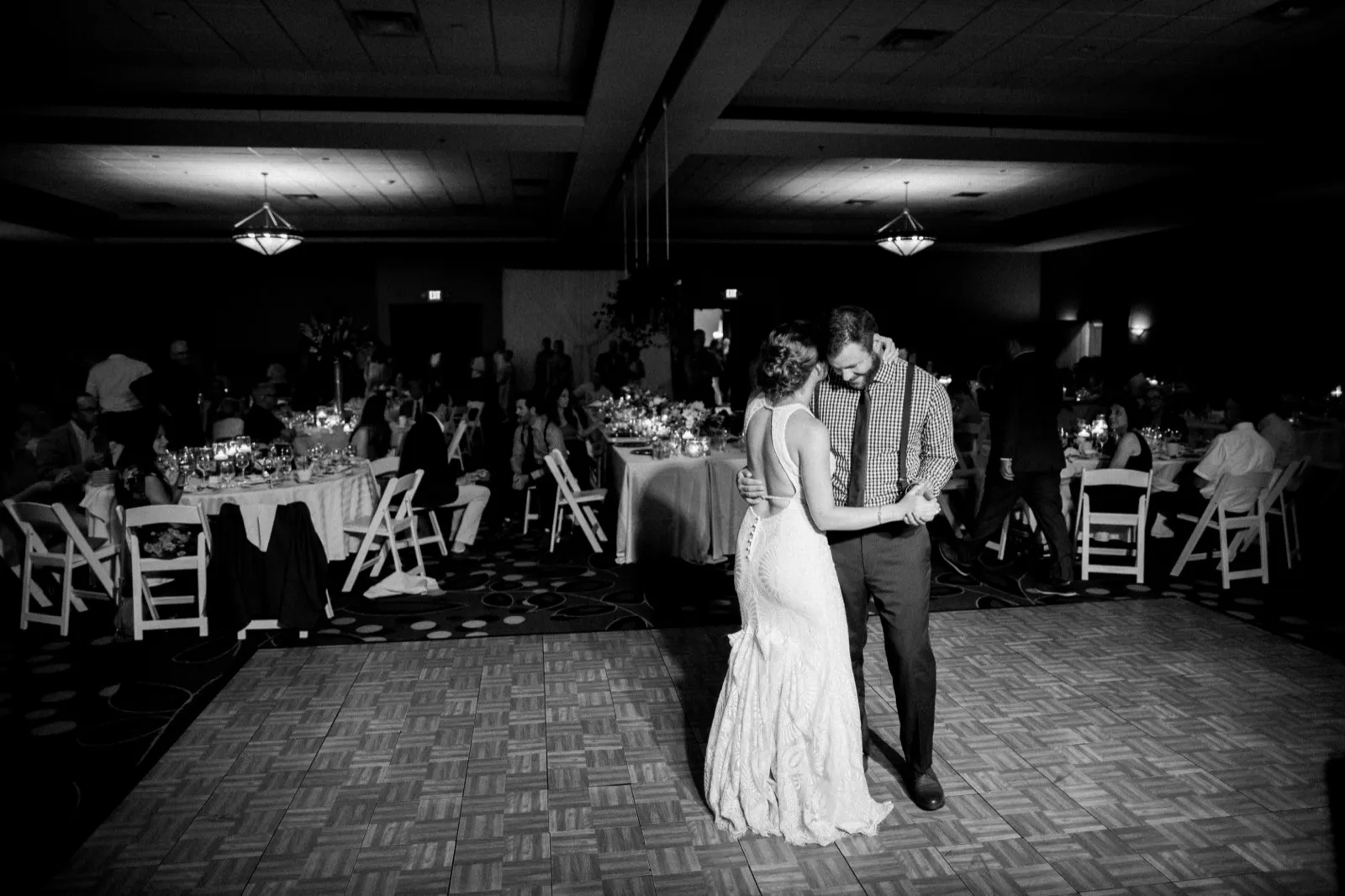 The bride and groom share their first dance on a parquet floor in a darkened ballroom, surrounded by seated guests at candlelit tables. — Tim Larsen Photography, Brainerd Lakes MN