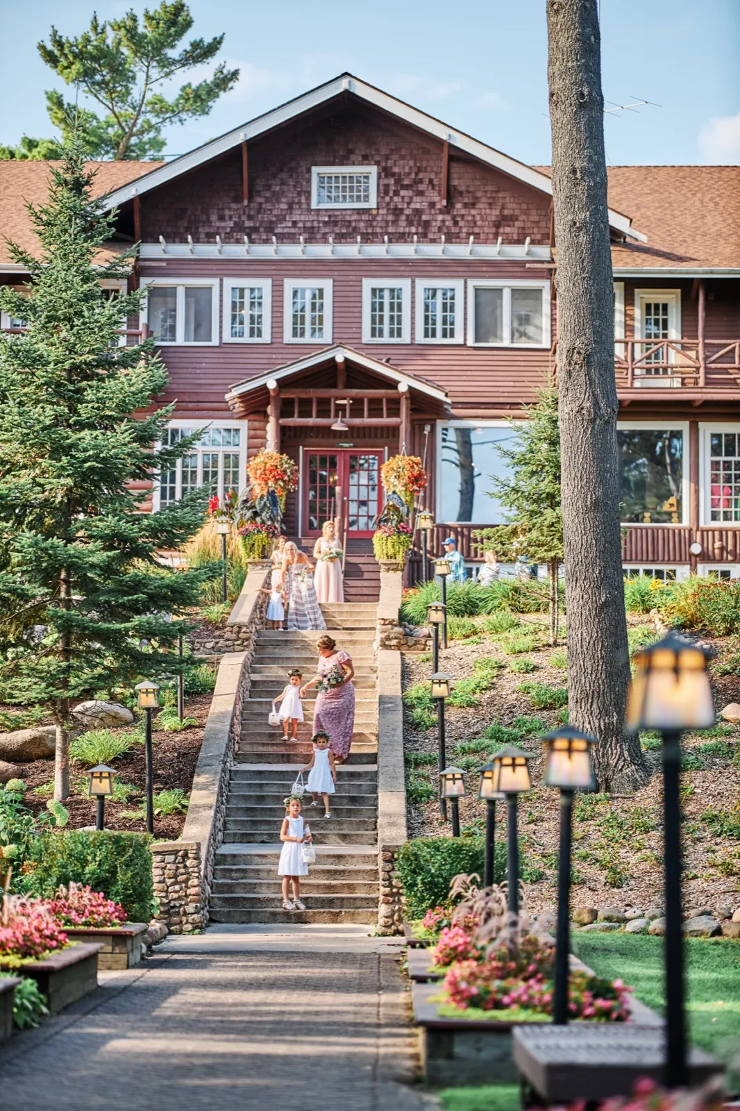The bridal party and flower girls walk down a wide stone stairway lined with lanterns in front of the timbered facade of Grand View Lodge. — Tim Larsen Photography, Brainerd Lakes MN