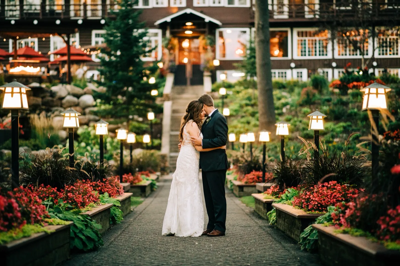 A couple embraces on a lantern-lined garden path at dusk in front of the glowing Grand View Lodge — Tim Larsen Photography, Brainerd Lakes MN