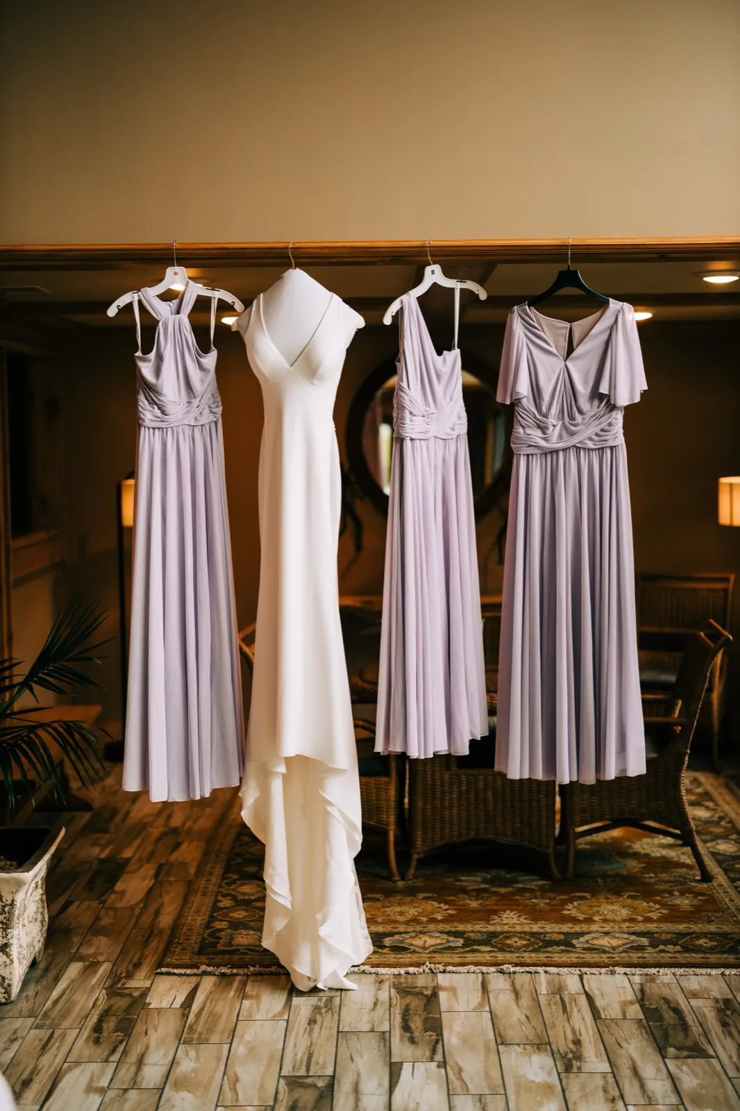 Katie's gown on a wooden beam flanked by three lavender bridesmaid dresses above a patterned rug — Tim Larsen Photography, Brainerd Lakes MN