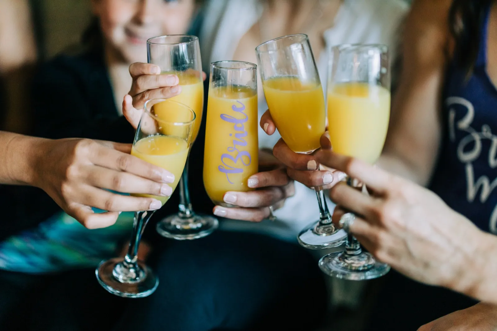 Four mimosa flutes meet in a getting-ready toast, one glass lettered 'Bride' in lavender script — Tim Larsen Photography, Brainerd Lakes MN