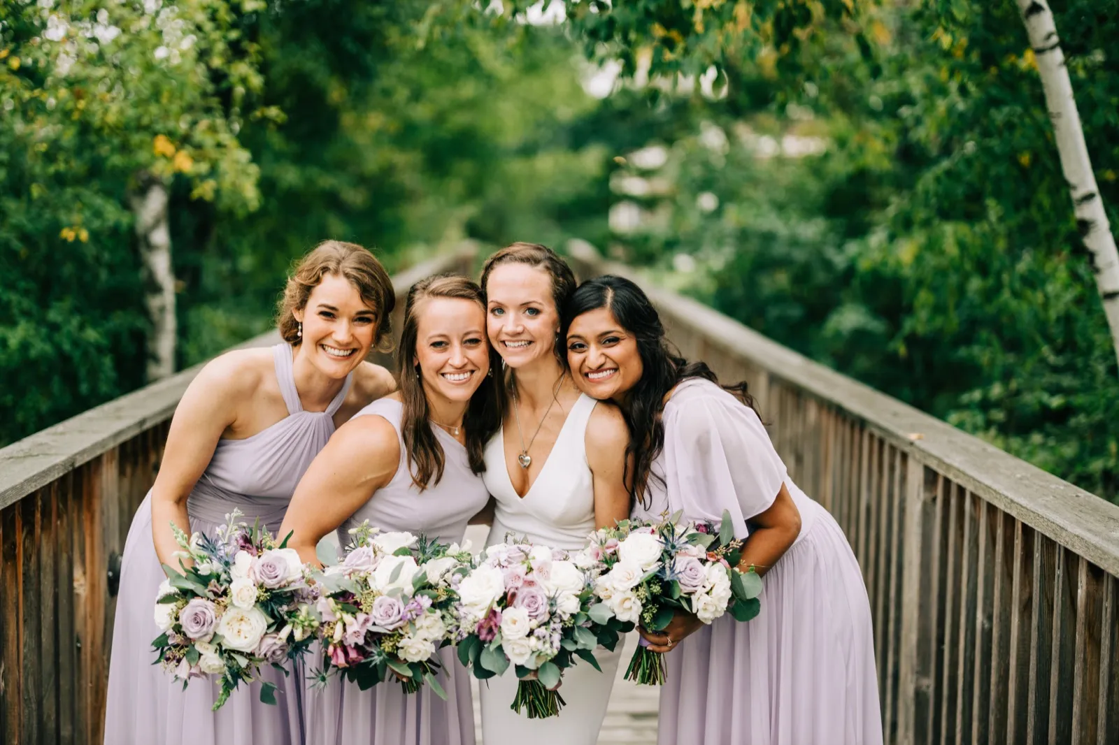 Katie leans in with three bridesmaids in lavender, bouquets pressed together, on a wooden footbridge at Madden's on Gull Lake — Tim Larsen Photography, Brainerd Lakes MN