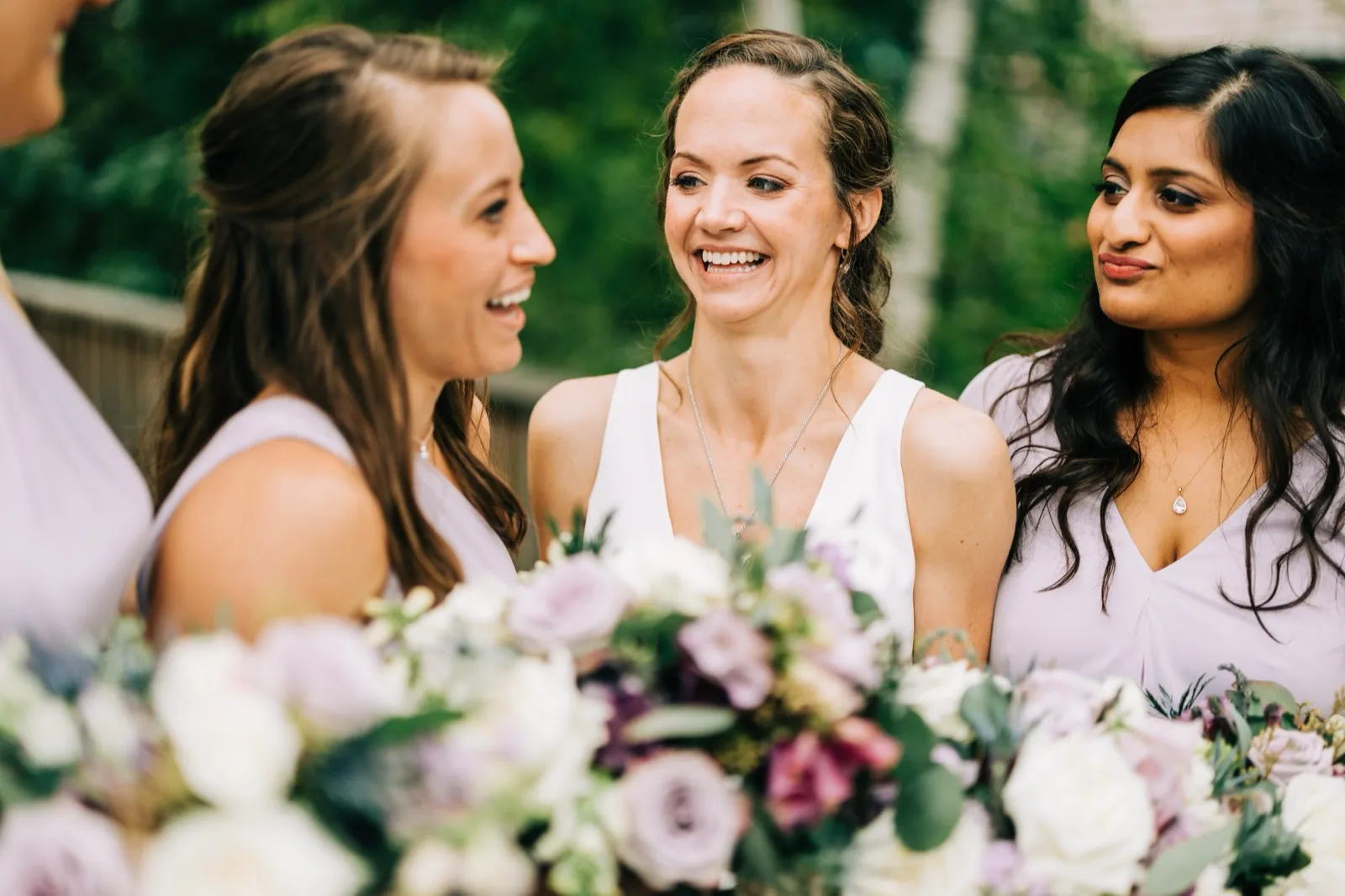Katie laughs with two bridesmaids in lavender, pastel bouquets framing the foreground — Tim Larsen Photography, Brainerd Lakes MN